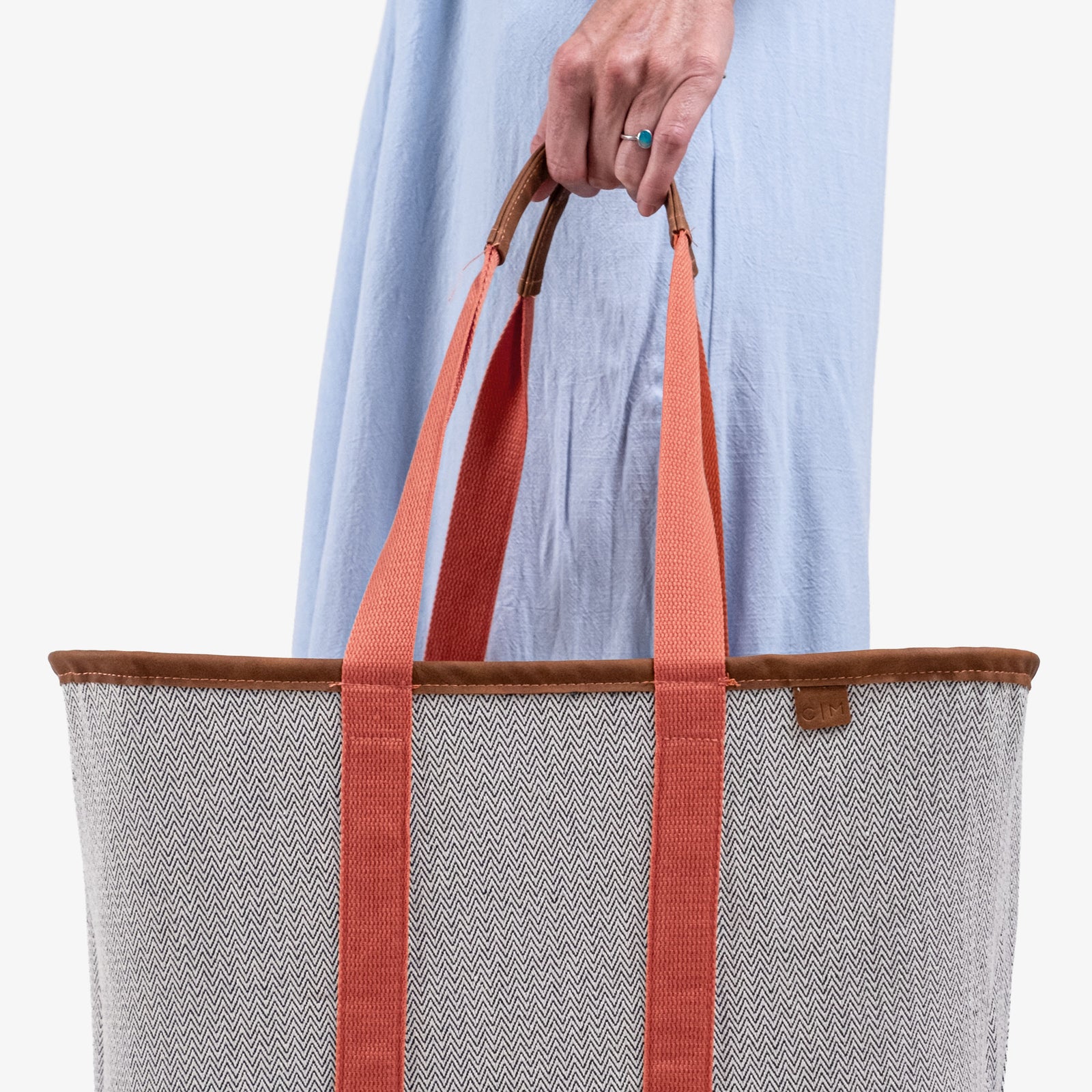 Person holding a tote bag with orange straps against a white background
