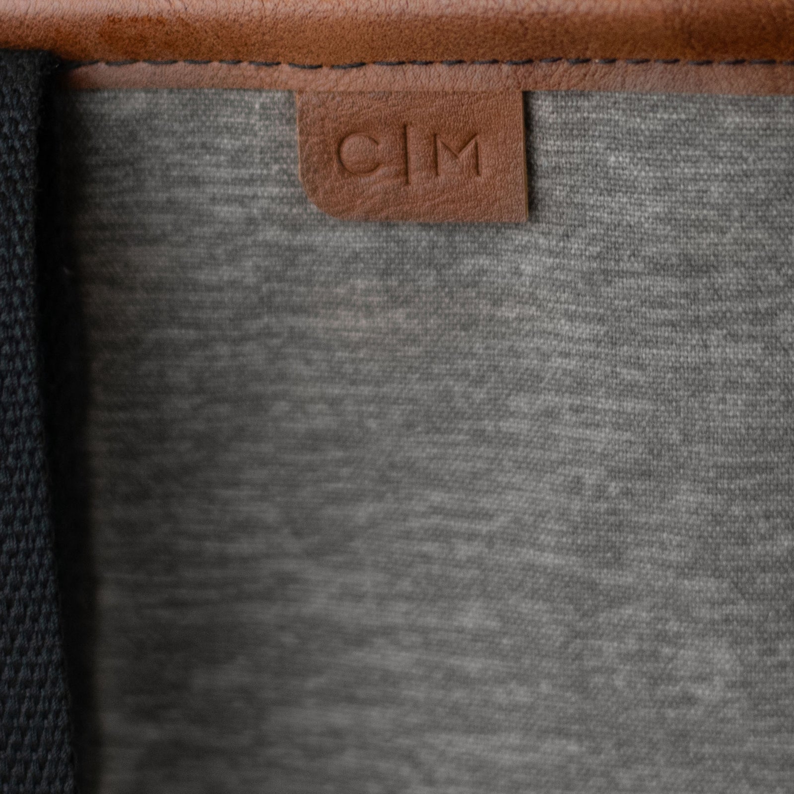 Close-up of a gray tote bag with a brown leather tag featuring 'C|M' branding.