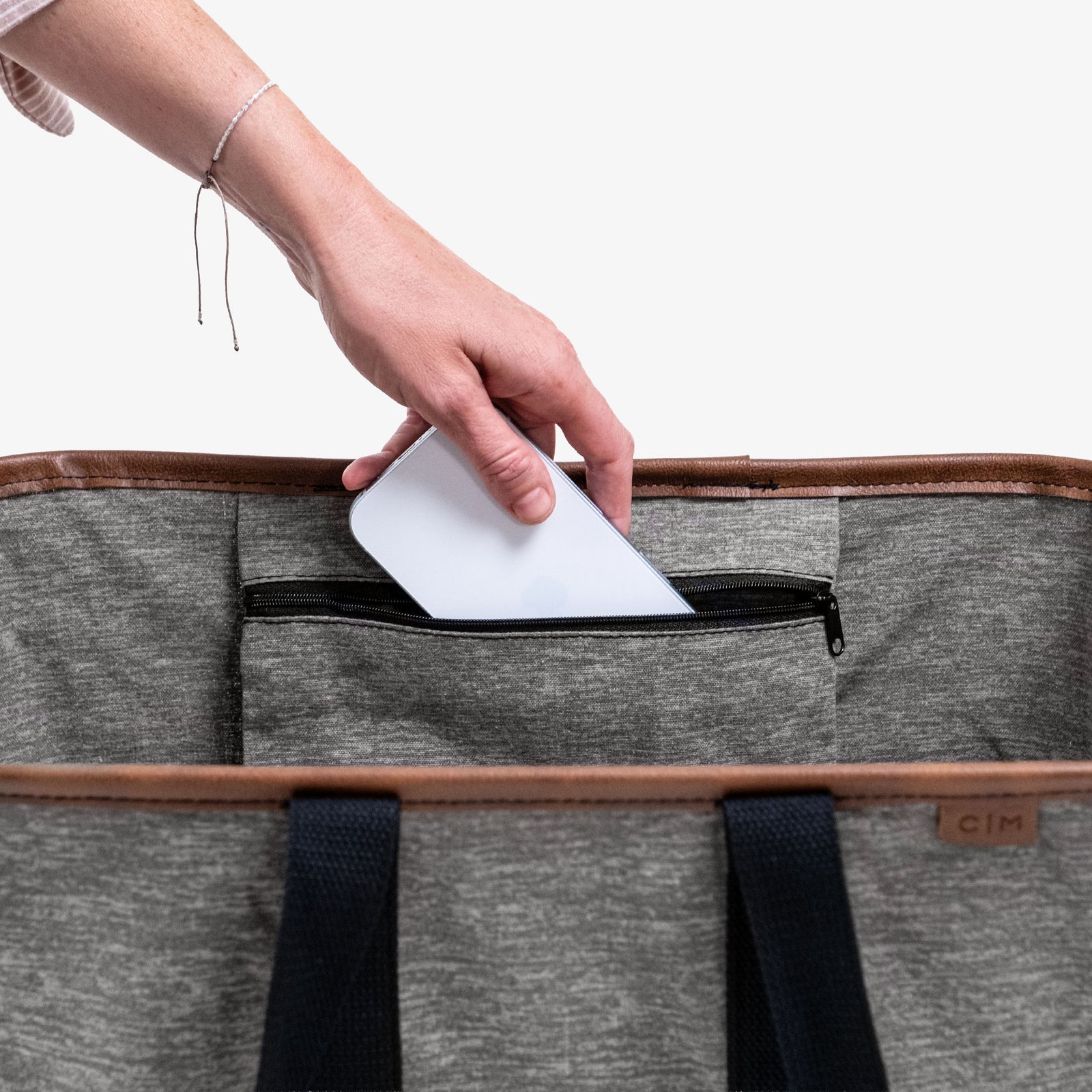 Person placing a white phone into a gray bag with black straps on a white background