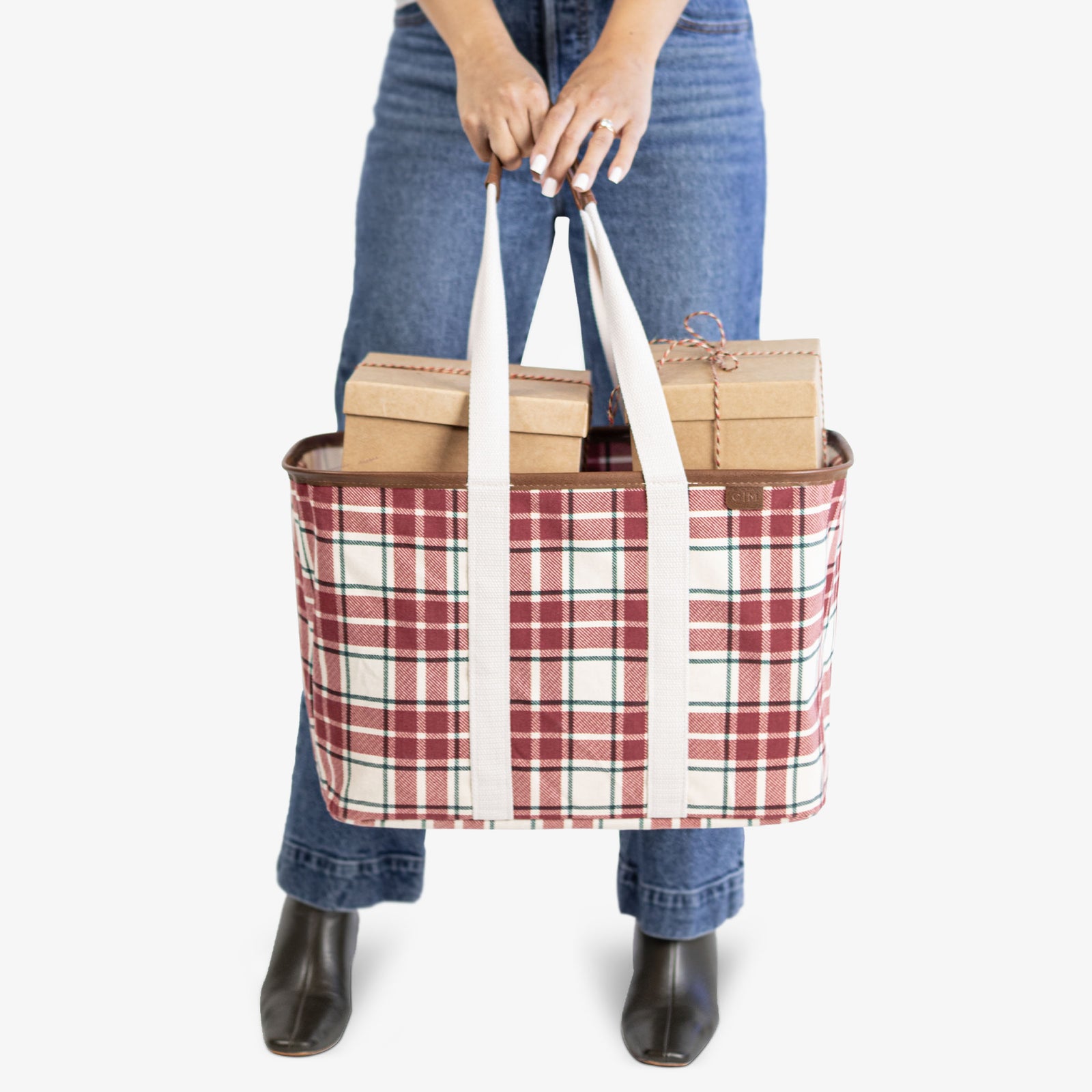 Person holding a plaid tote bag with boxes inside on a white background