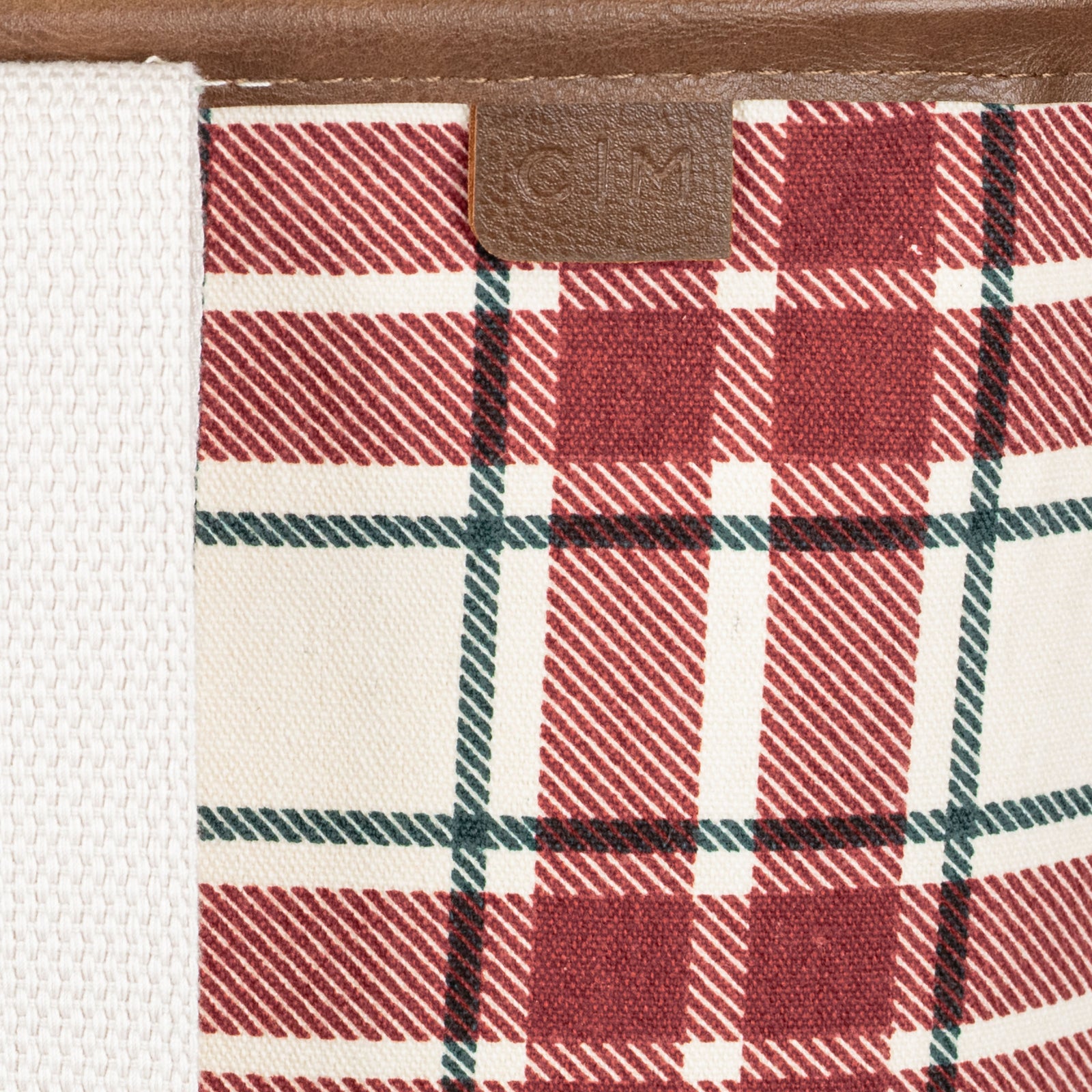 Close-up of a red and white plaid patterned tote bag with a brand label on a brown background.