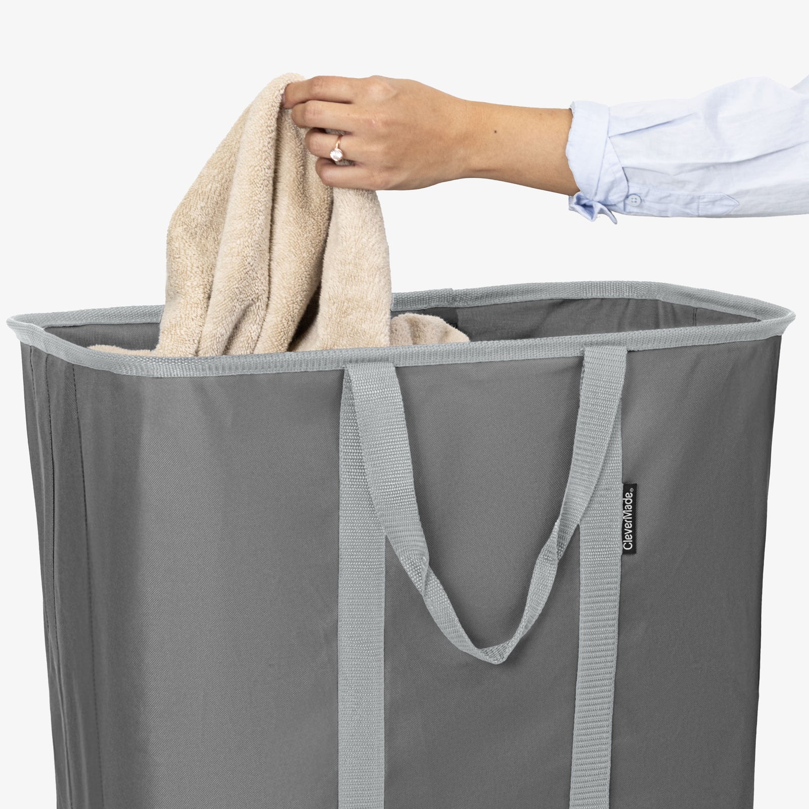 Person placing a towel into a gray laundry basket with a visible brand logo.