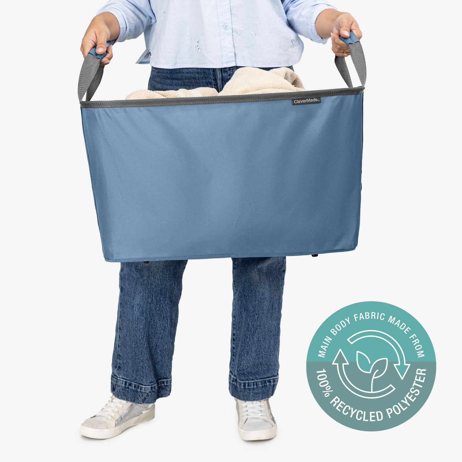 Person holding a large blue laundry basket with a label indicating 100% recycled polyester.
