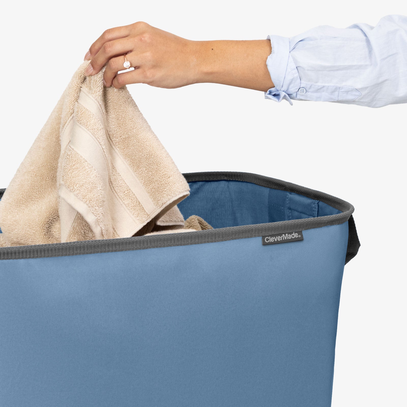 Person placing a towel into a blue CleverMade laundry basket.