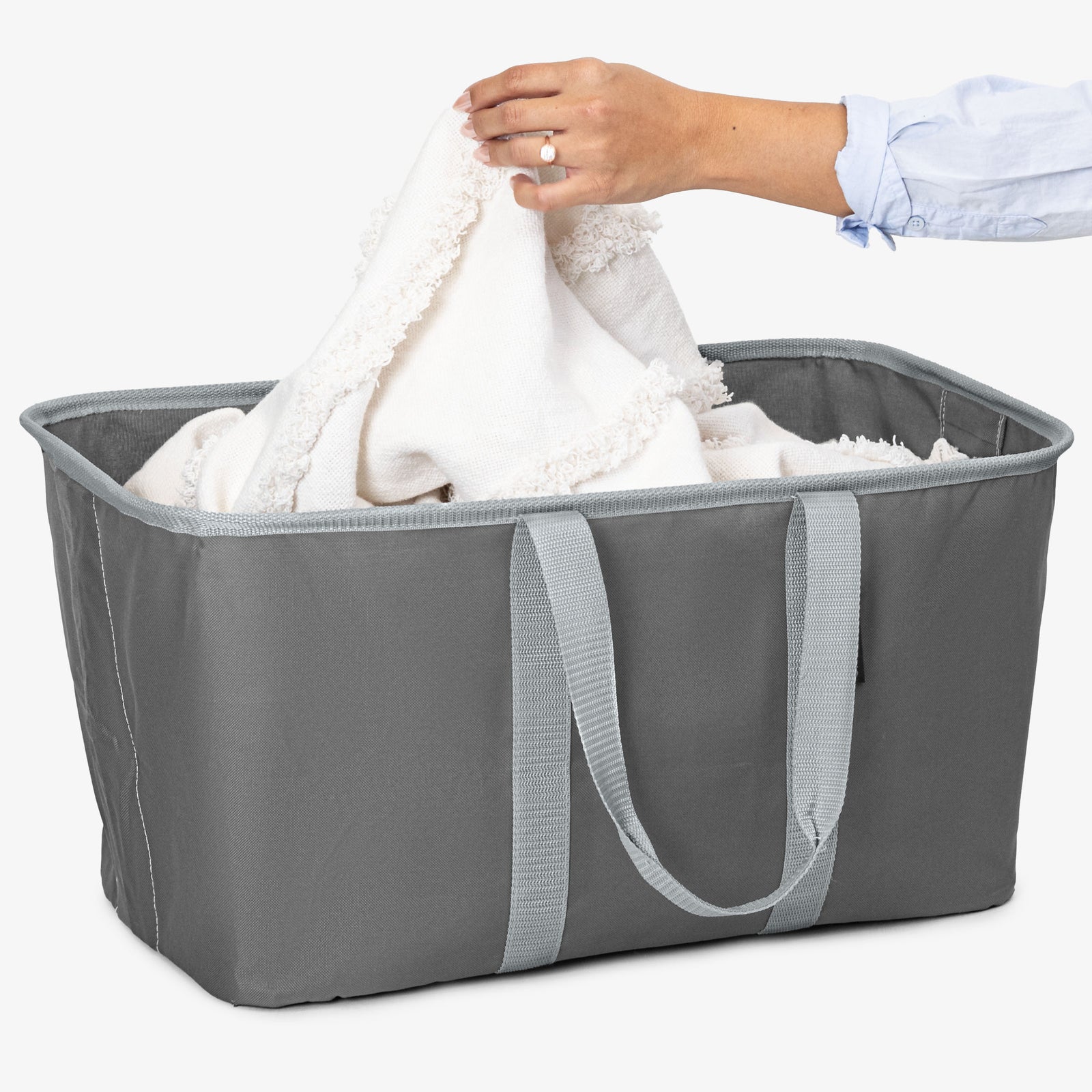 Person placing a white towel into a gray laundry basket on a white background