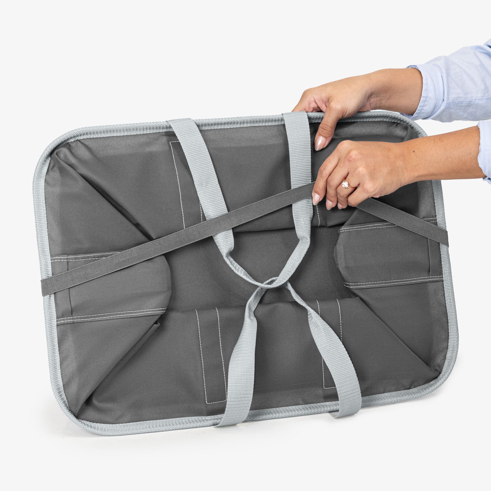 Gray laundry tote bag with straps being adjusted by a person on a white background
