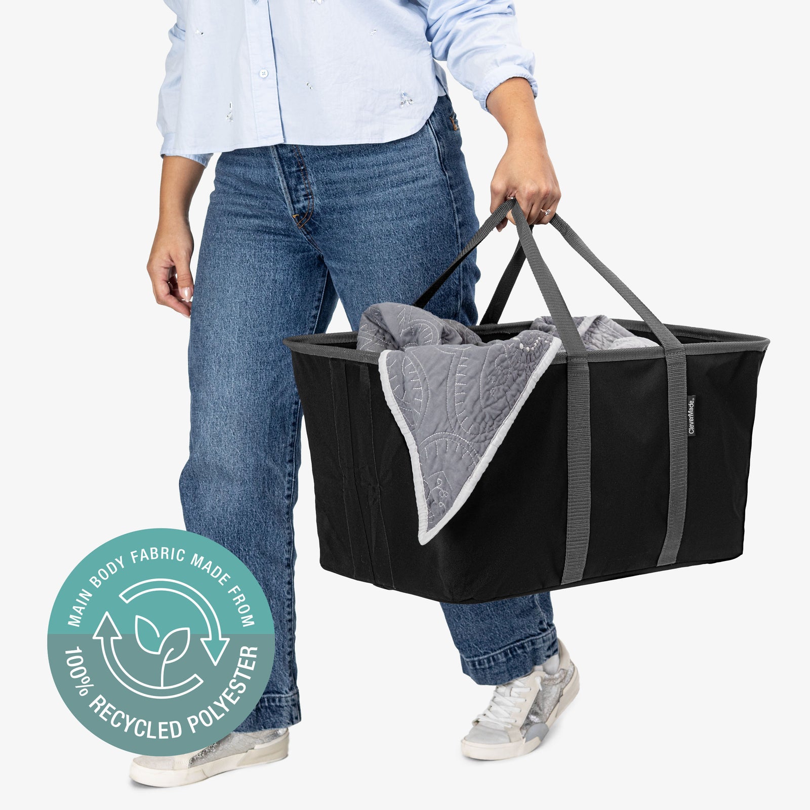 Person holding a black carrying basket with a gray blanket, featuring a circular green label with text on a white background.