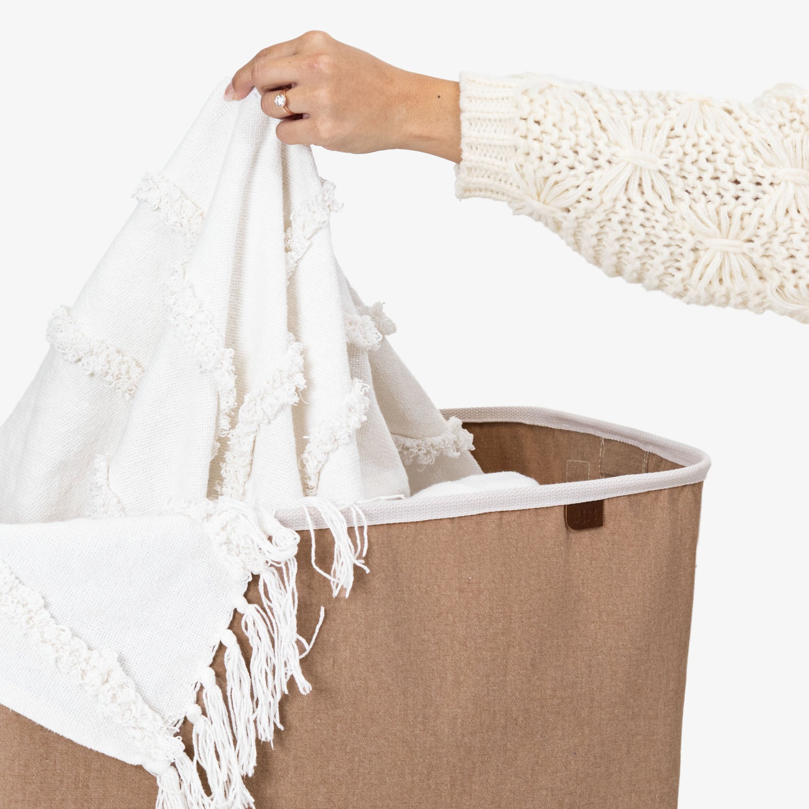 Person holding a white towel with fringe over a beige laundry basket.