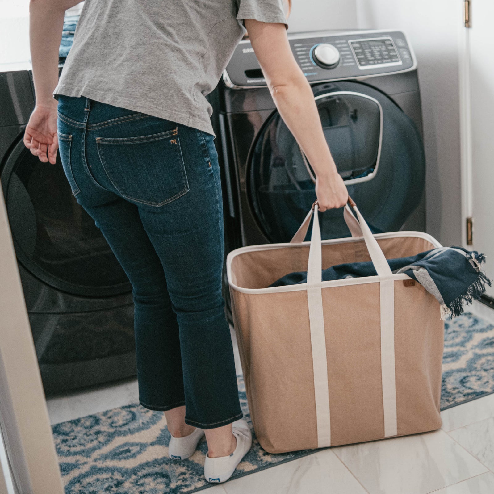 Person holding a large brown tote bag in front of a washing machine