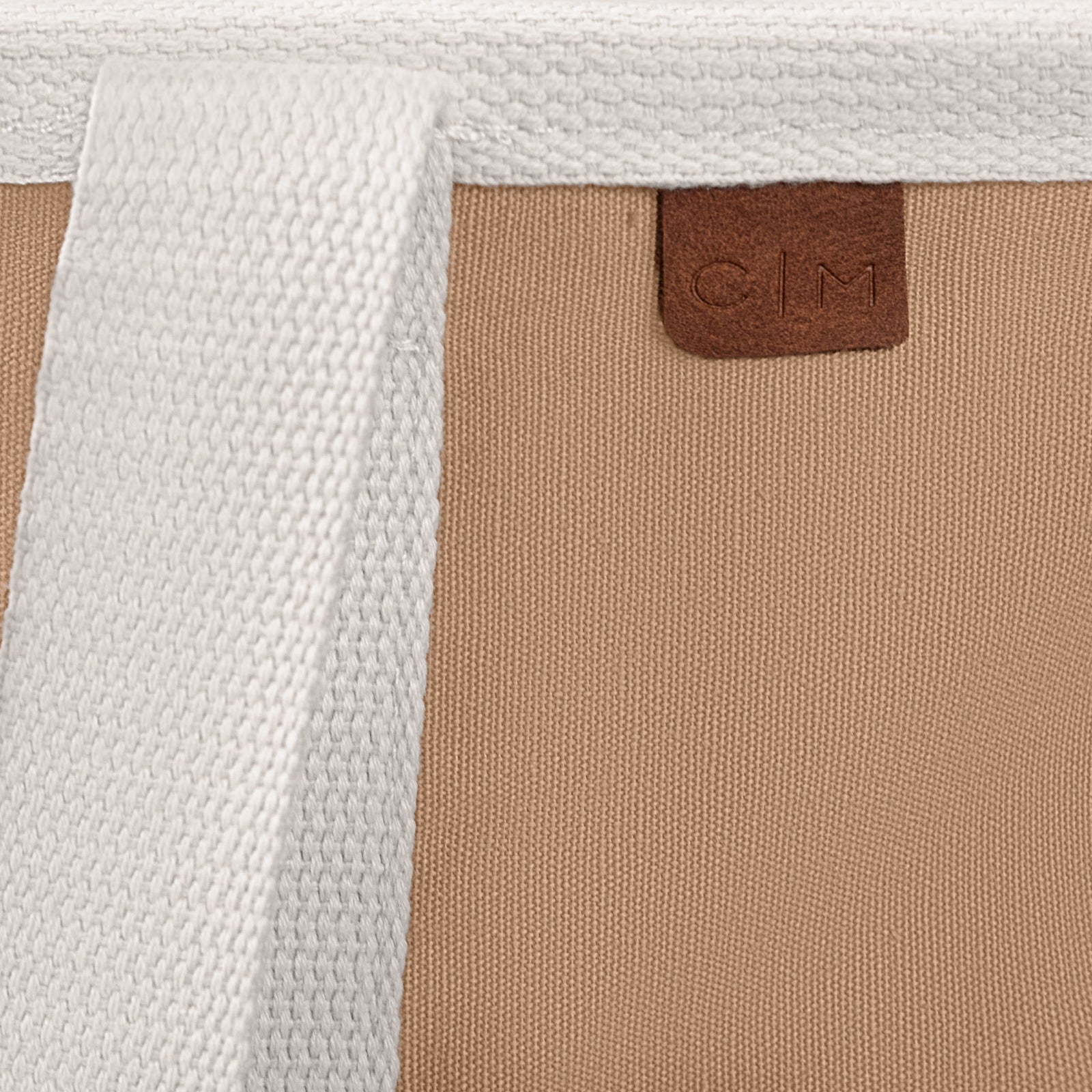 Close-up of a laundry caddy LUXE bag with a brown label featuring 'C|M' on a beige and white textured background.