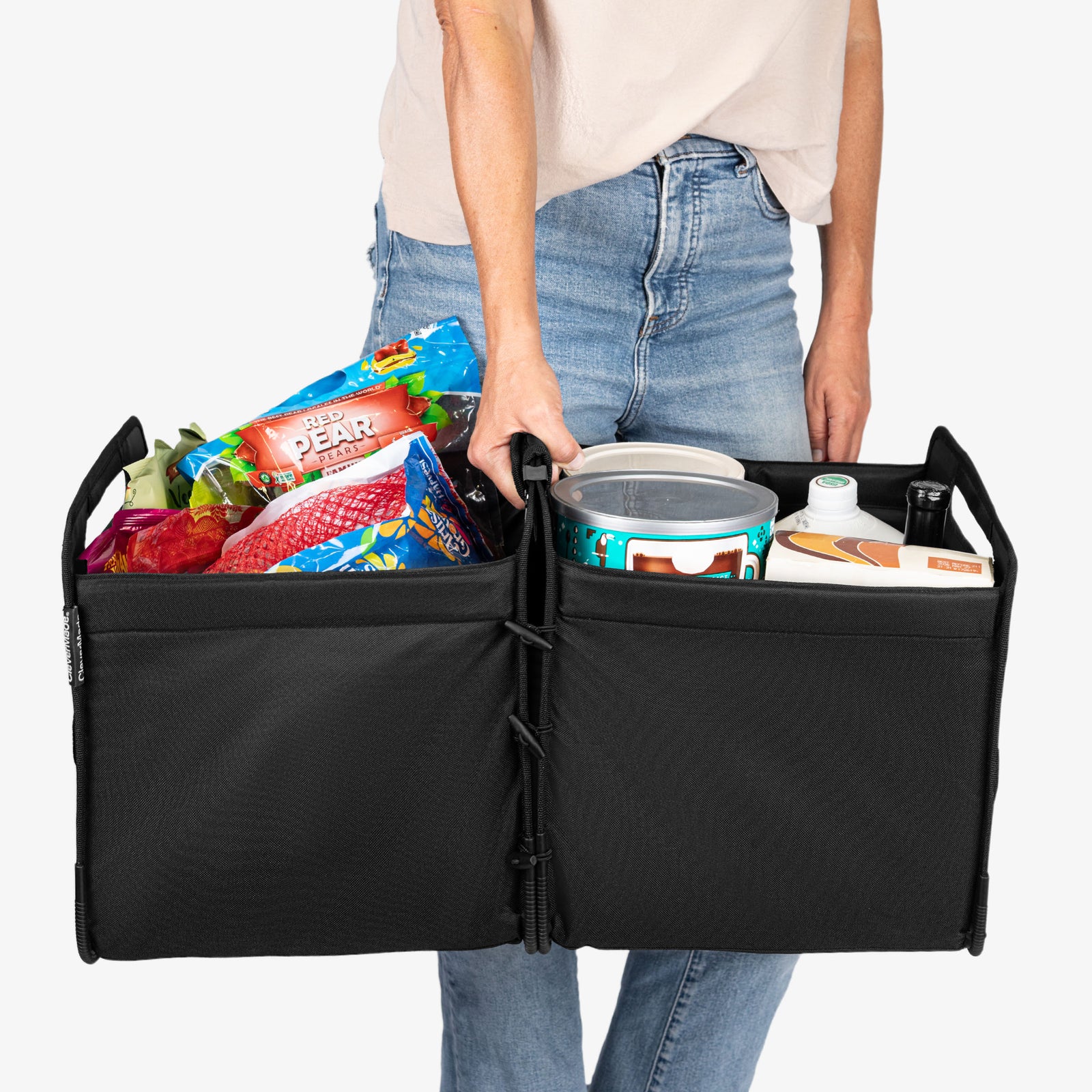 Person holding a black folding trunk caddy with groceries inside on a white background