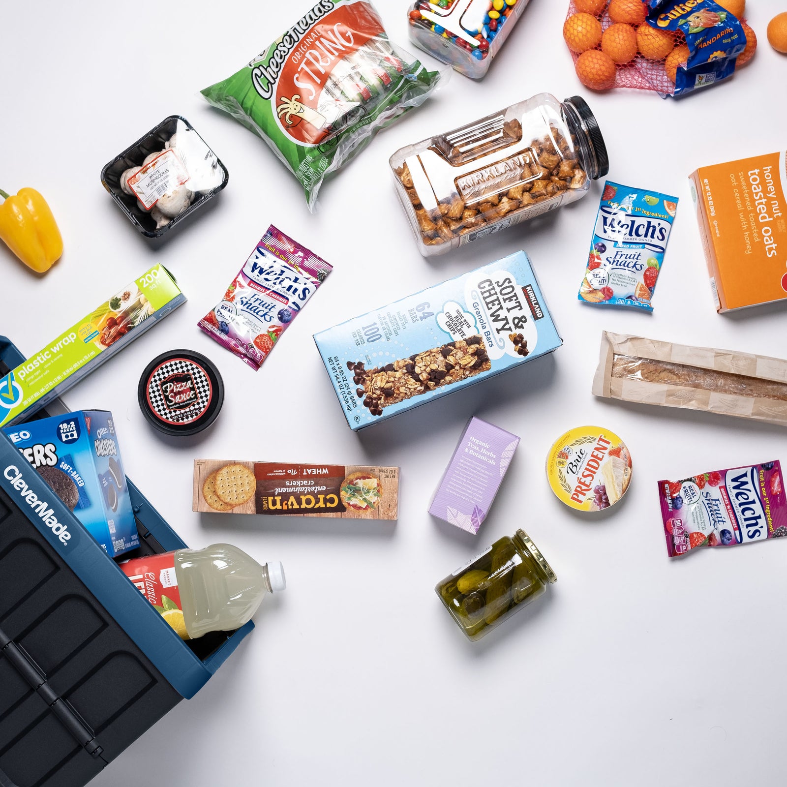 A blue and black collapsible storage bin with lid with assorted snacks and food items on a white surface