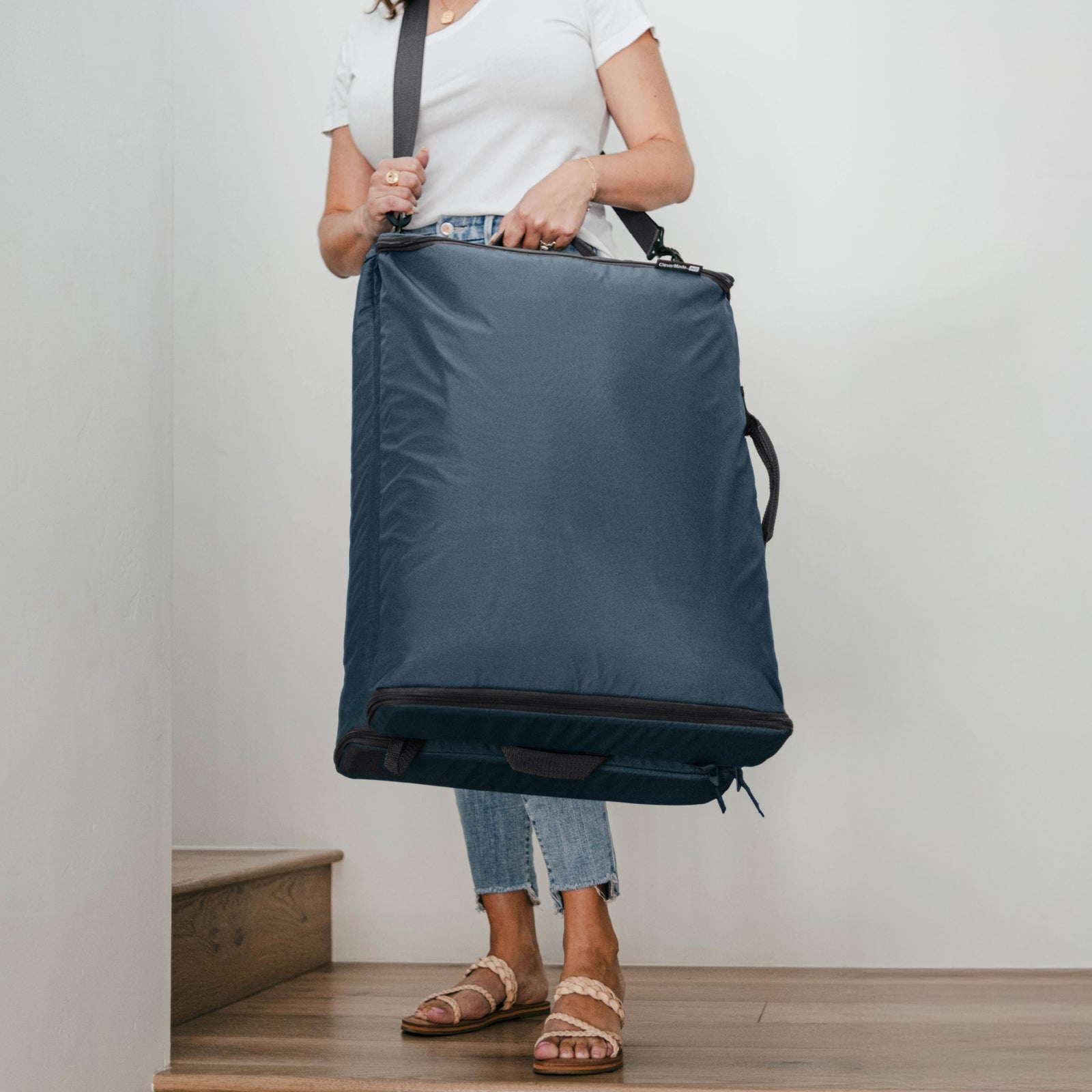Person carrying a folded blue Convertible Laundry Hamper with a shoulder strap and a grab handle.