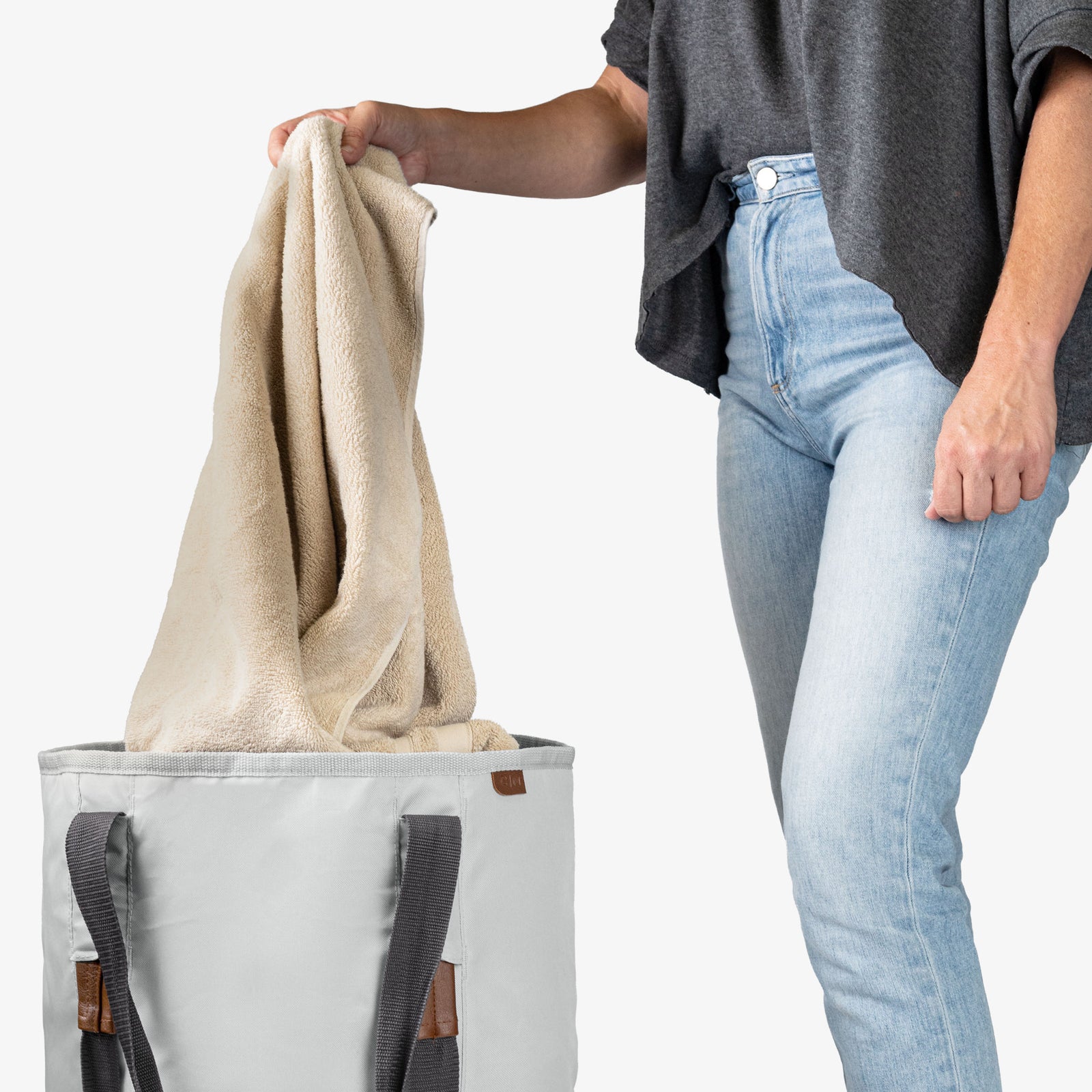 Person holding a beige towel above a charcoal laundry backpack duffel bag
on a white background