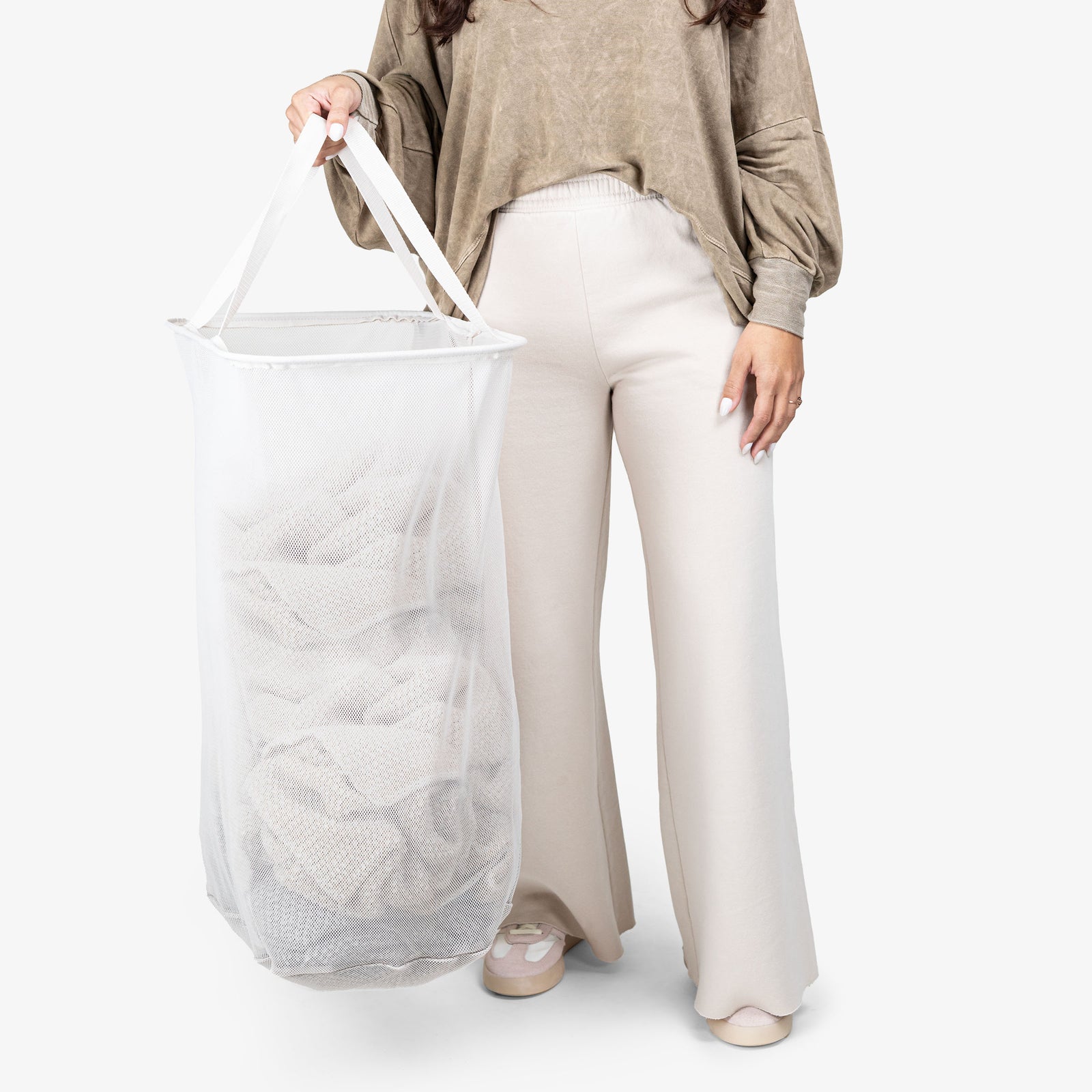 Person holding a large white mesh laundry bag against a plain background