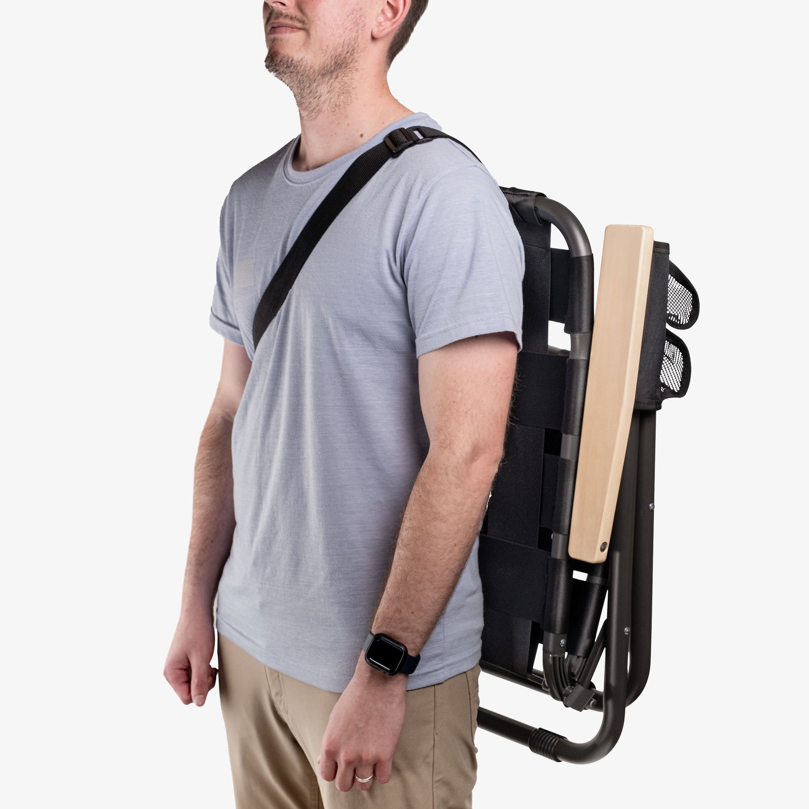 Person carrying folded black Kove outdoor chair with strap over shoulder