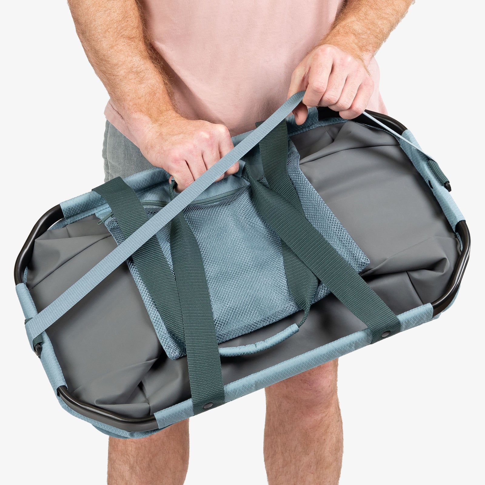 Person holding a gray duffel bag with green straps on a white background