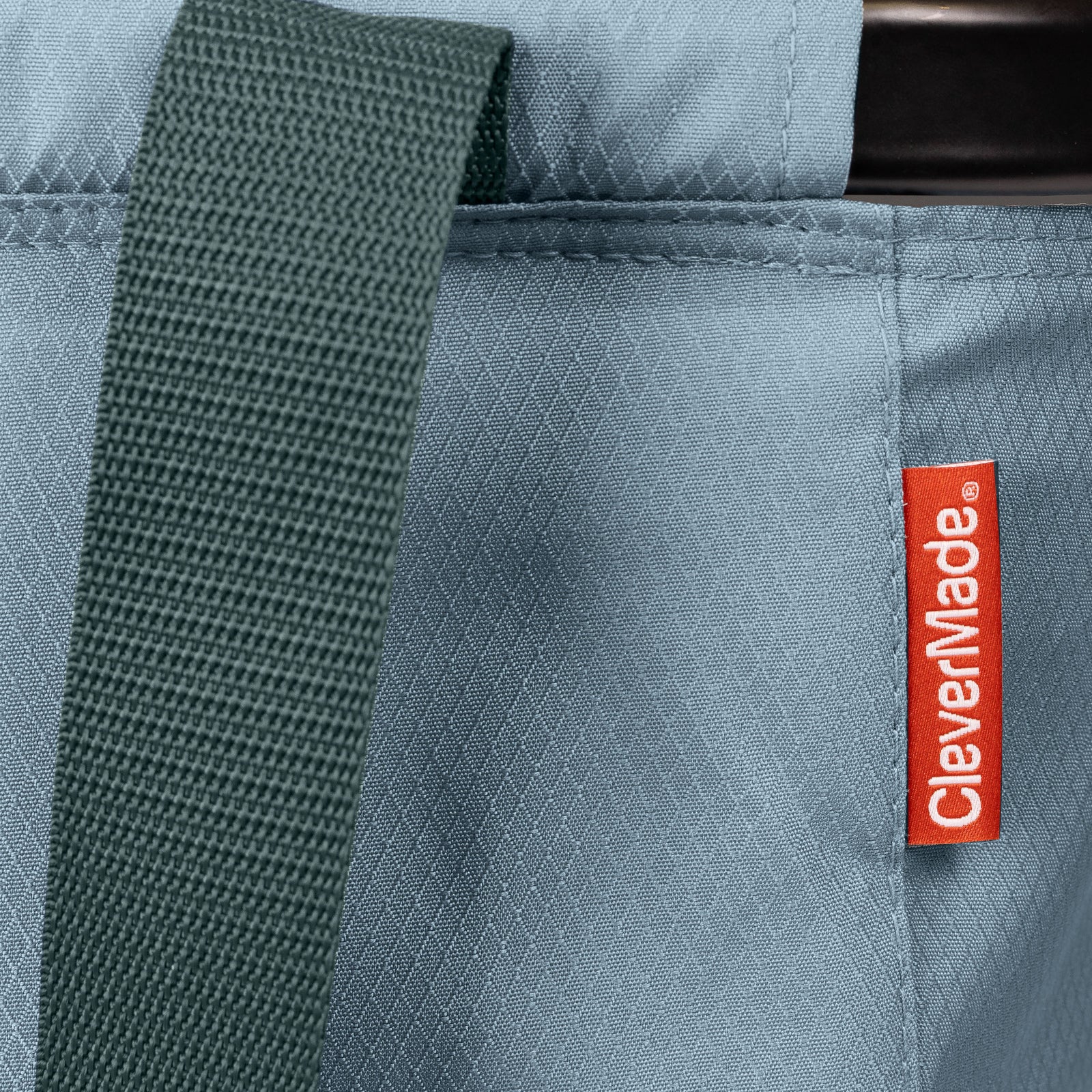 Close-up of a blue bag with a green strap and CleverMade label.