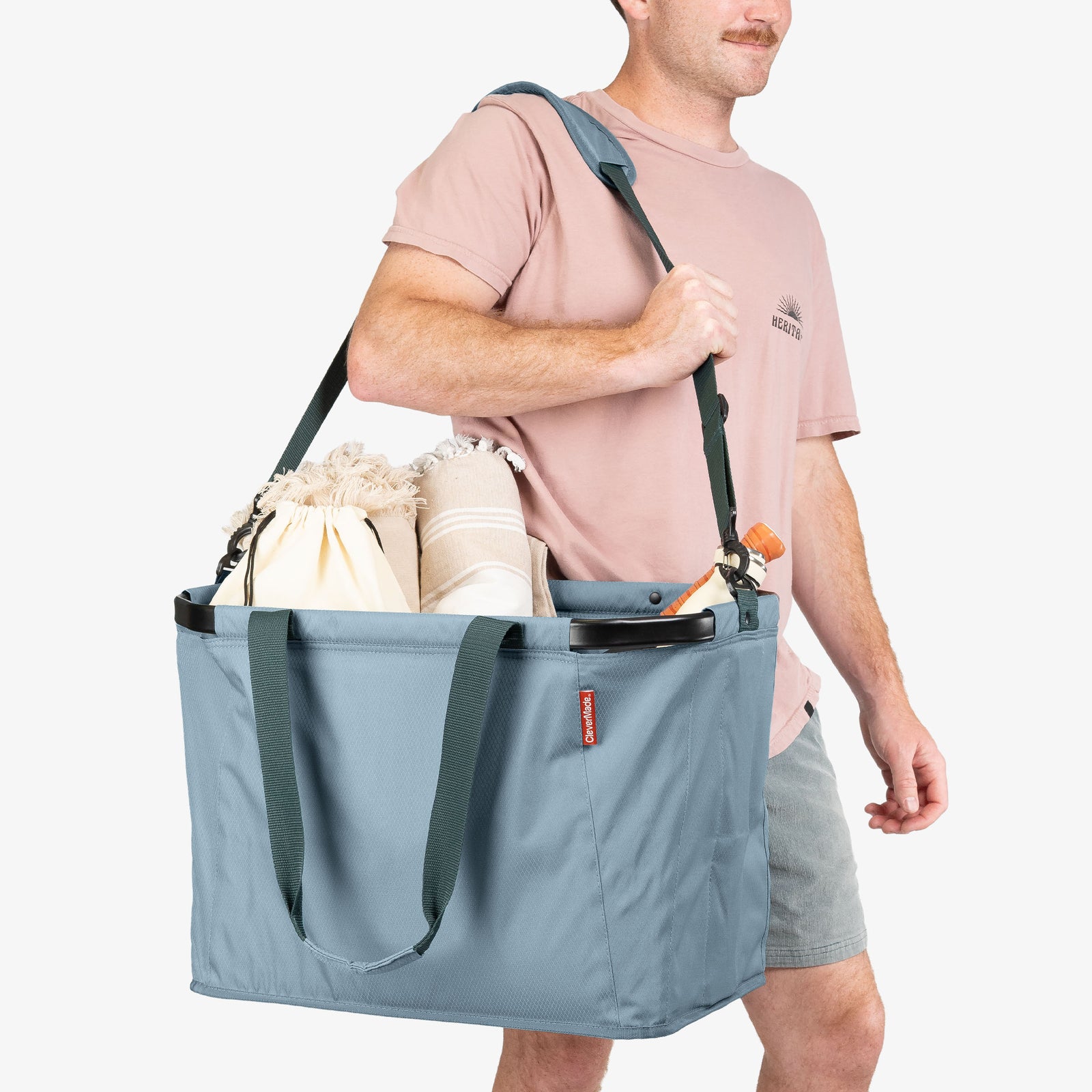 Person carrying a large blue tote bag filled with items on a white background