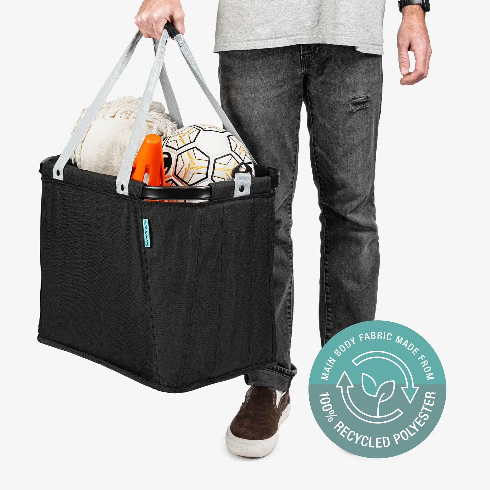 Person holding a black tote bag with sports equipment, featuring a label indicating 100% recycled polyester.