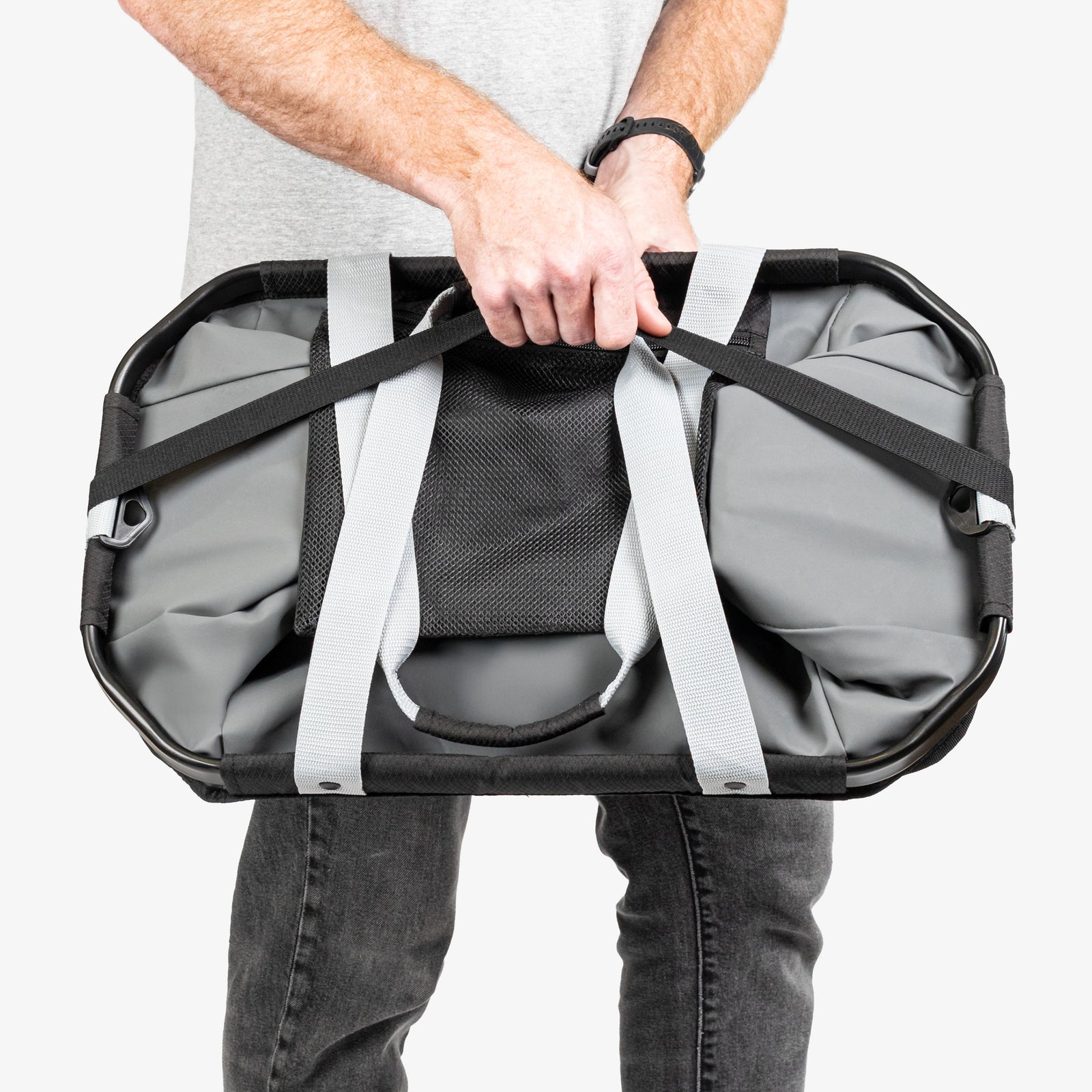 Person holding a large gray duffel bag with straps on a white background