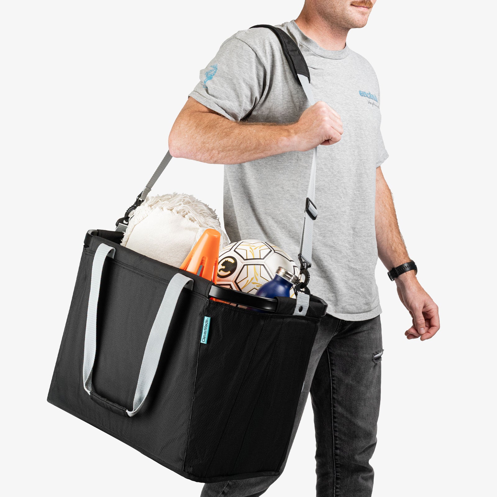 Person carrying a black sports bag filled with soccer balls and equipment on a white background