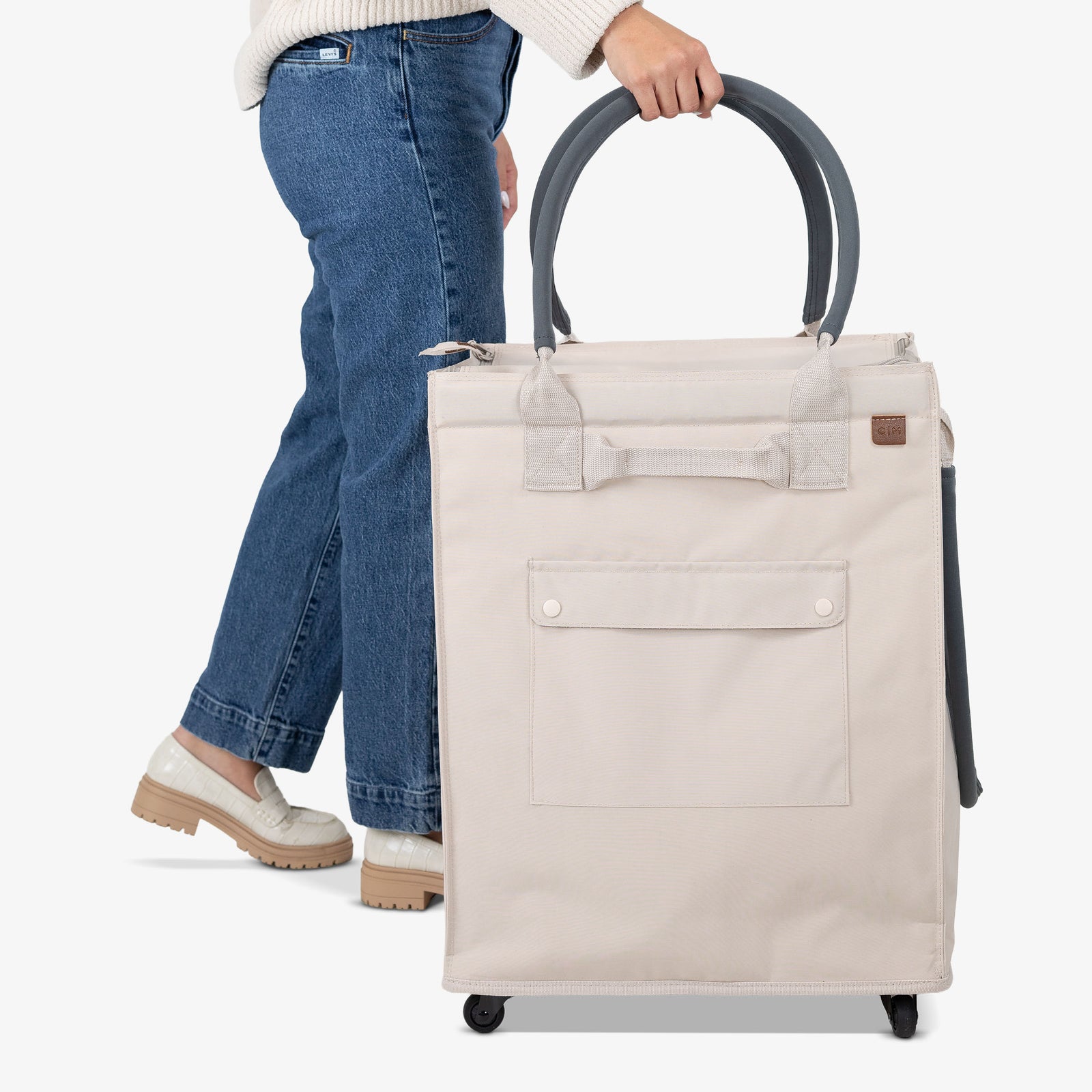 Person holding a beige rolling tote bag on a white background