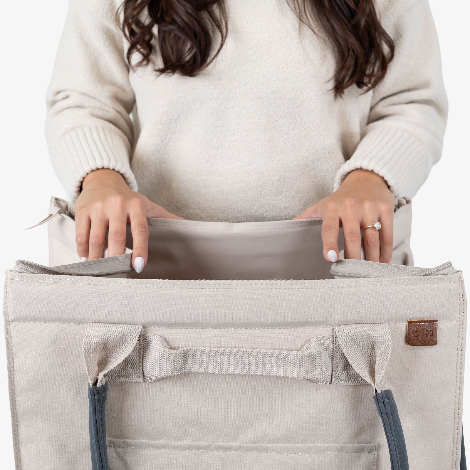 Person holding a beige tote bag with blue straps on a white background