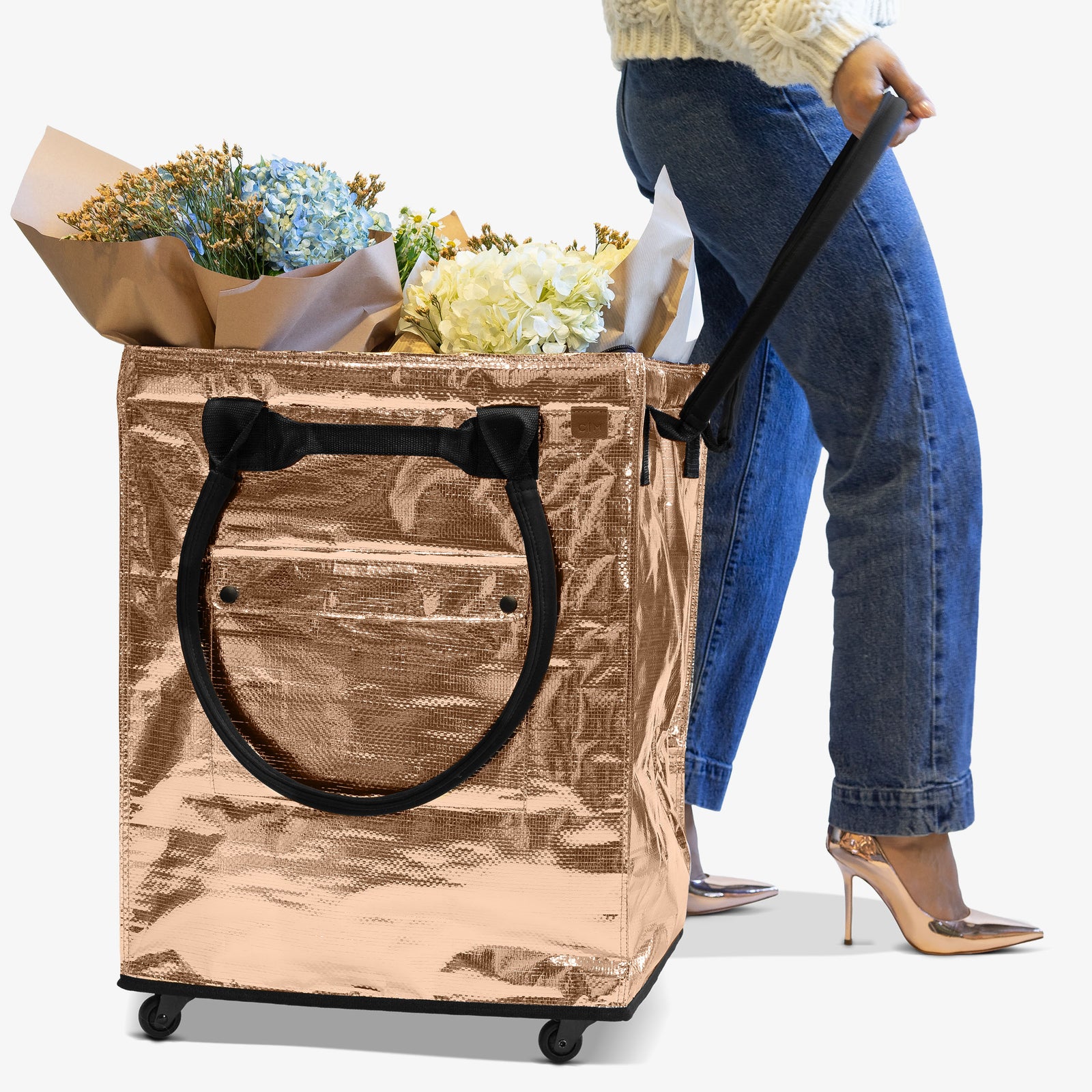 Person pulling a large metallic shopping bag filled with flowers on wheels.