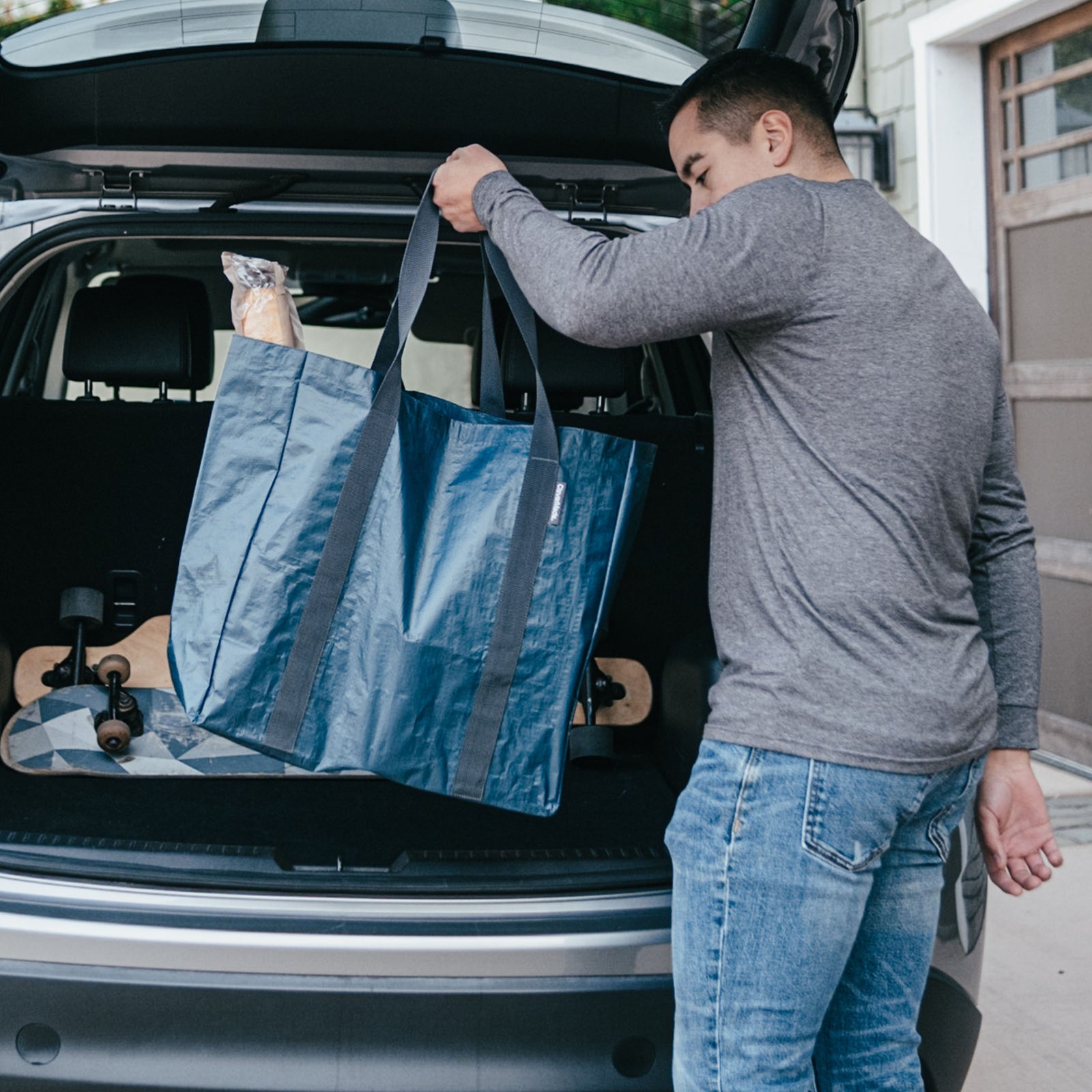 Man loading a blue reusable storage tote bag into the trunk of a car