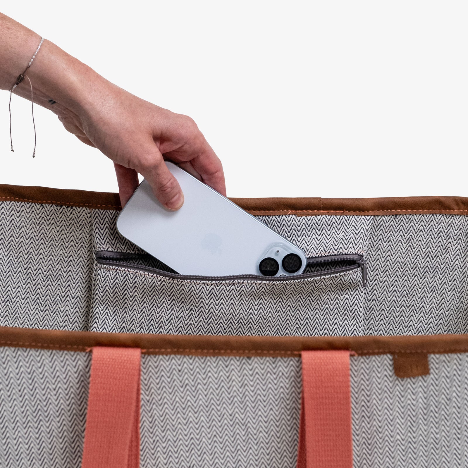 Hand placing a white electronic device into a gray tote bag with brown straps.