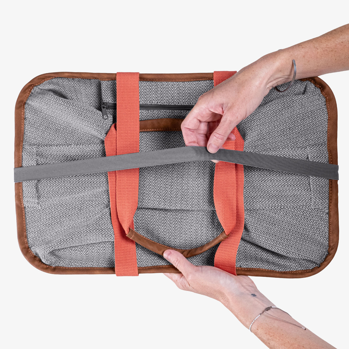 Person holding a gray tote bag with orange straps on a white background