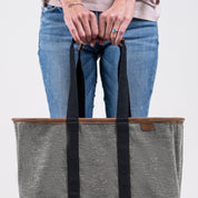 Person holding a gray tote bag with black straps on a light gray background