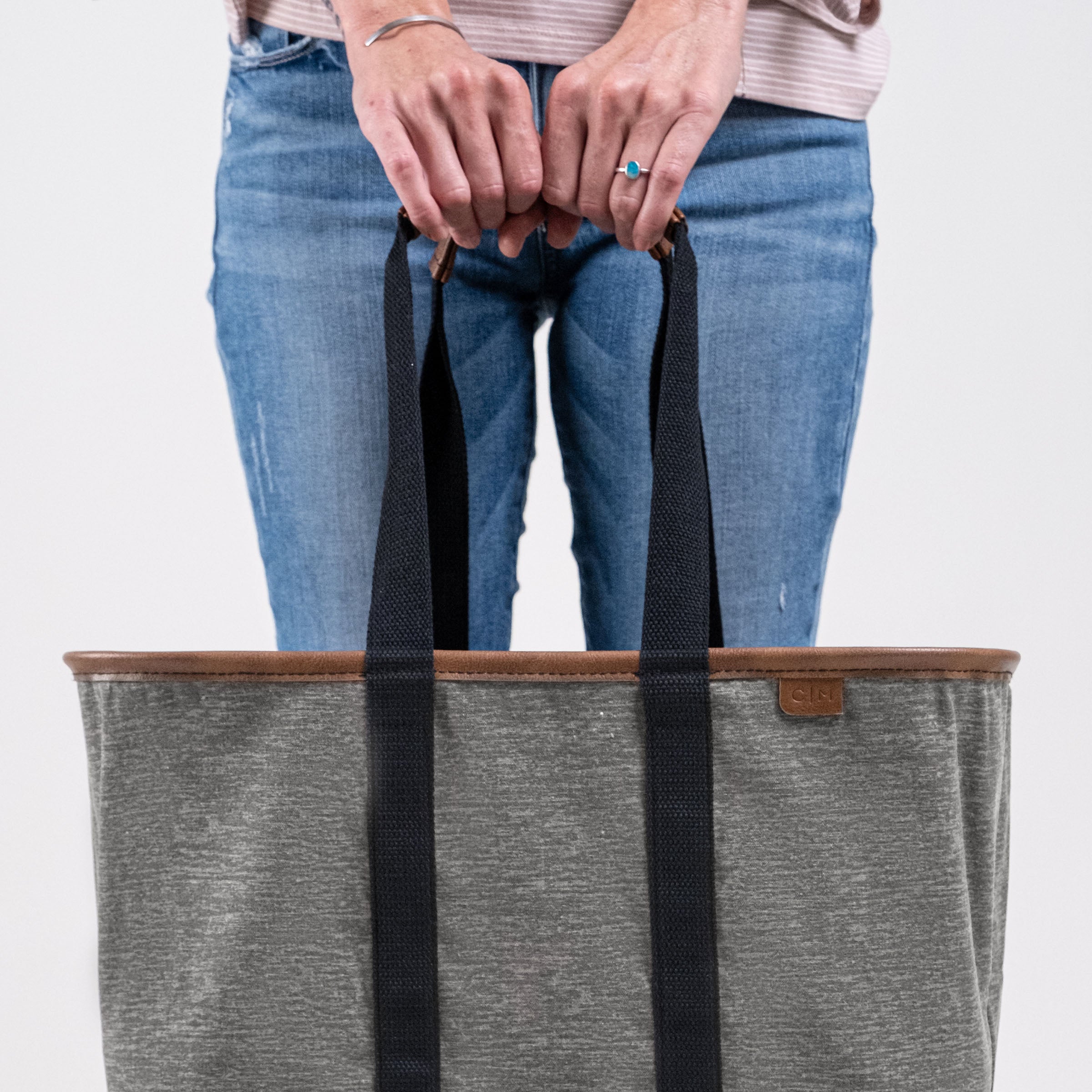 Person holding a gray tote bag with black straps on a light gray background