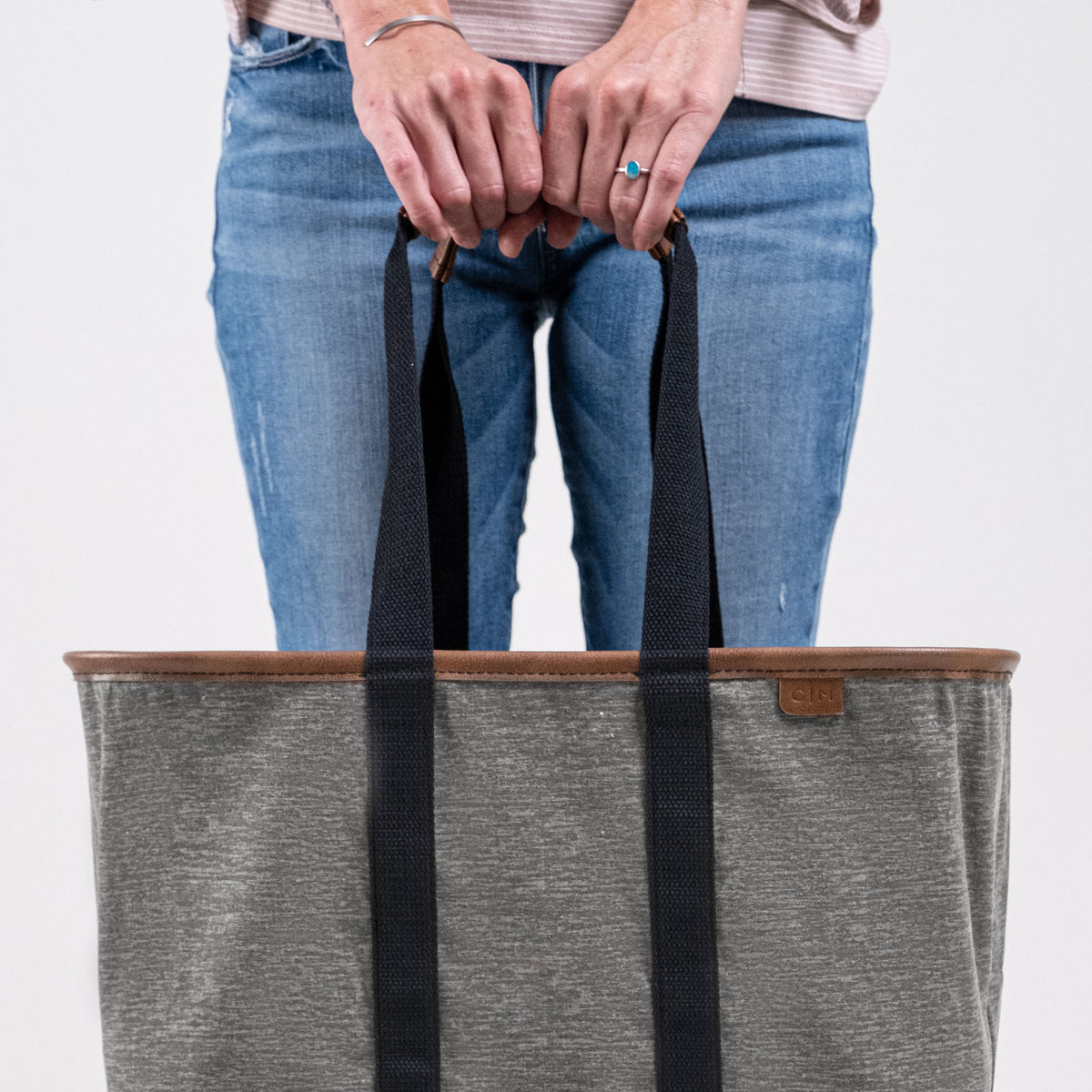 Person holding a gray tote bag with black straps on a light gray background