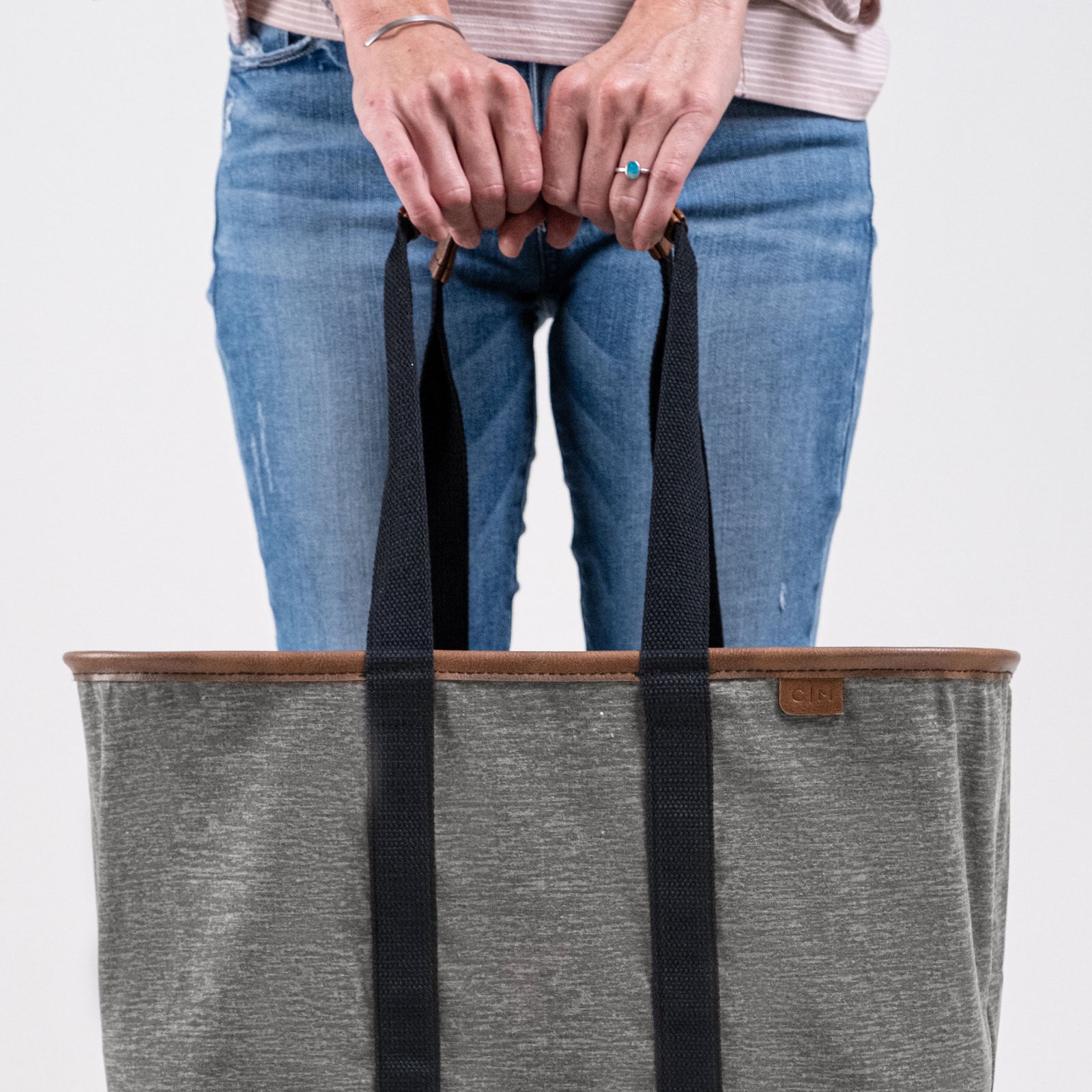 Person holding a gray tote bag with black straps on a light gray background