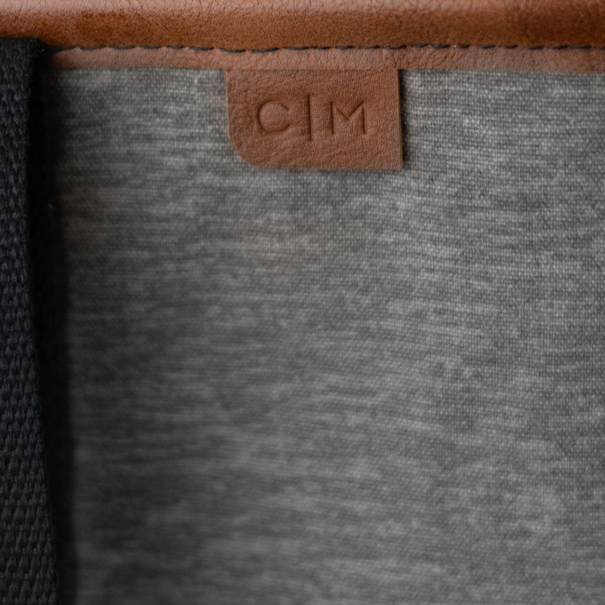 Close-up of a gray tote bag with a brown leather tag featuring 'C|M' branding.