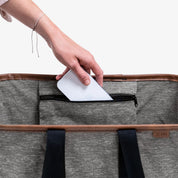 Person placing a white phone into a gray bag with black straps on a white background