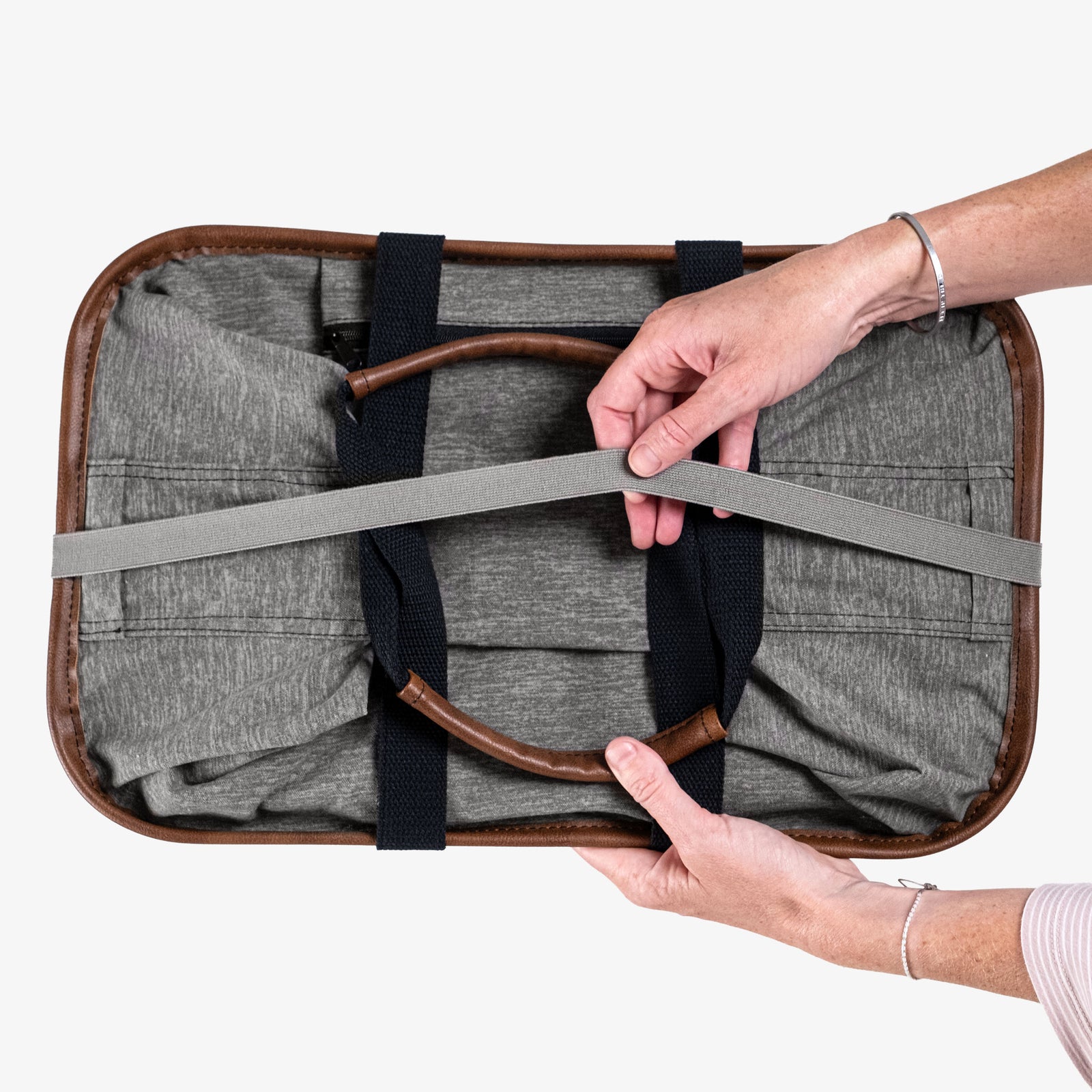 Person holding a gray tote bag with brown leather trim against a white background