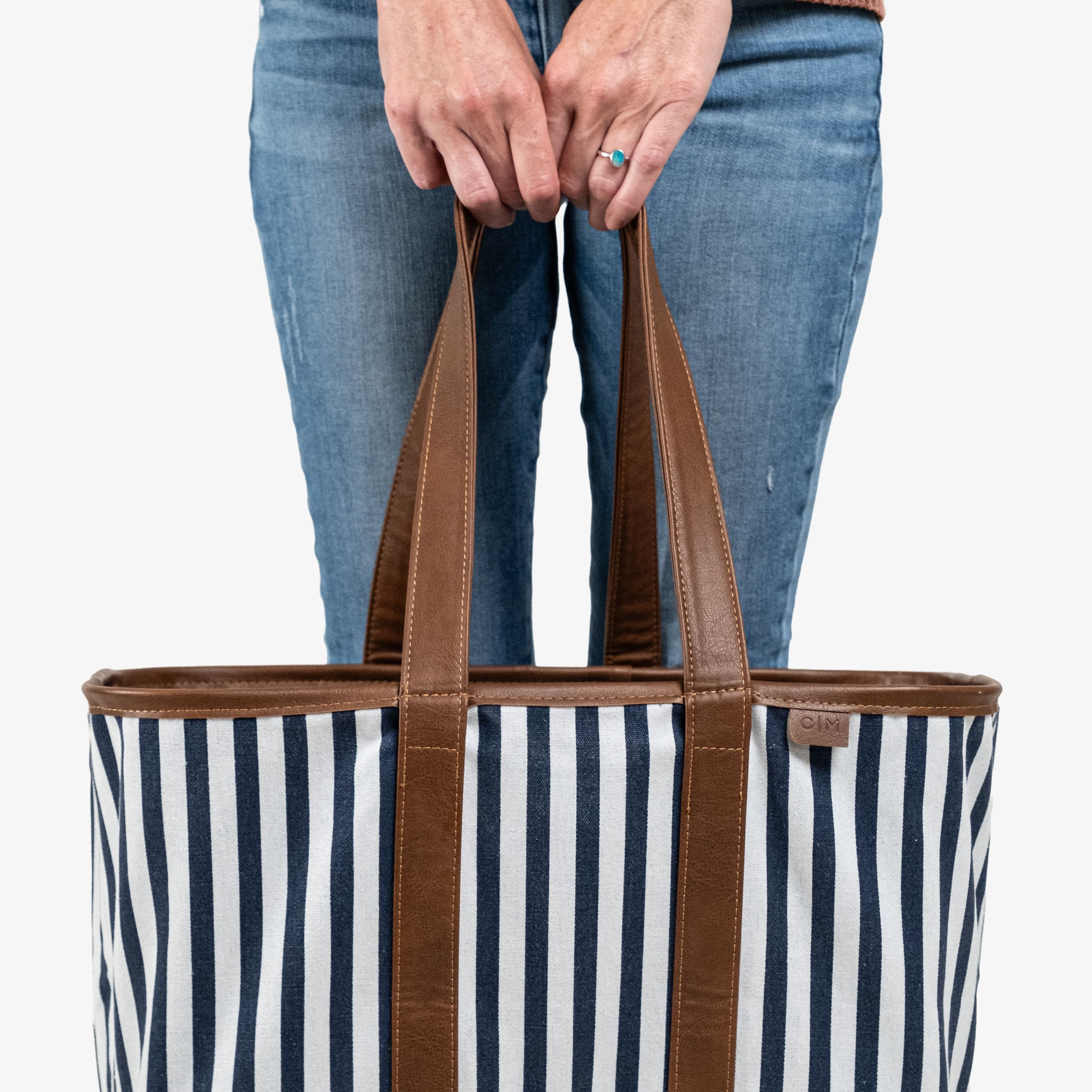 Person holding a striped tote bag with brown handles on a white background