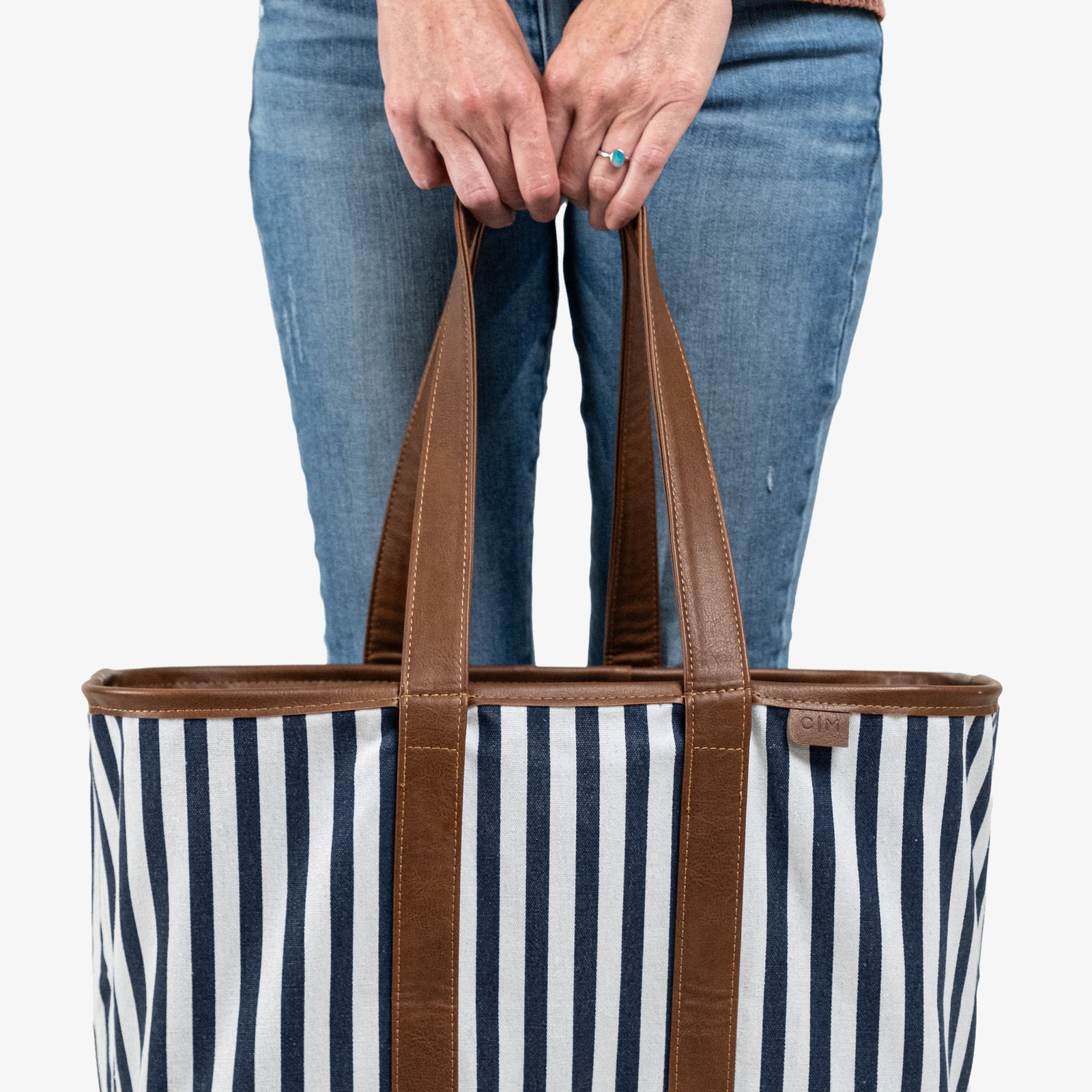 Person holding a striped tote bag with brown handles on a white background