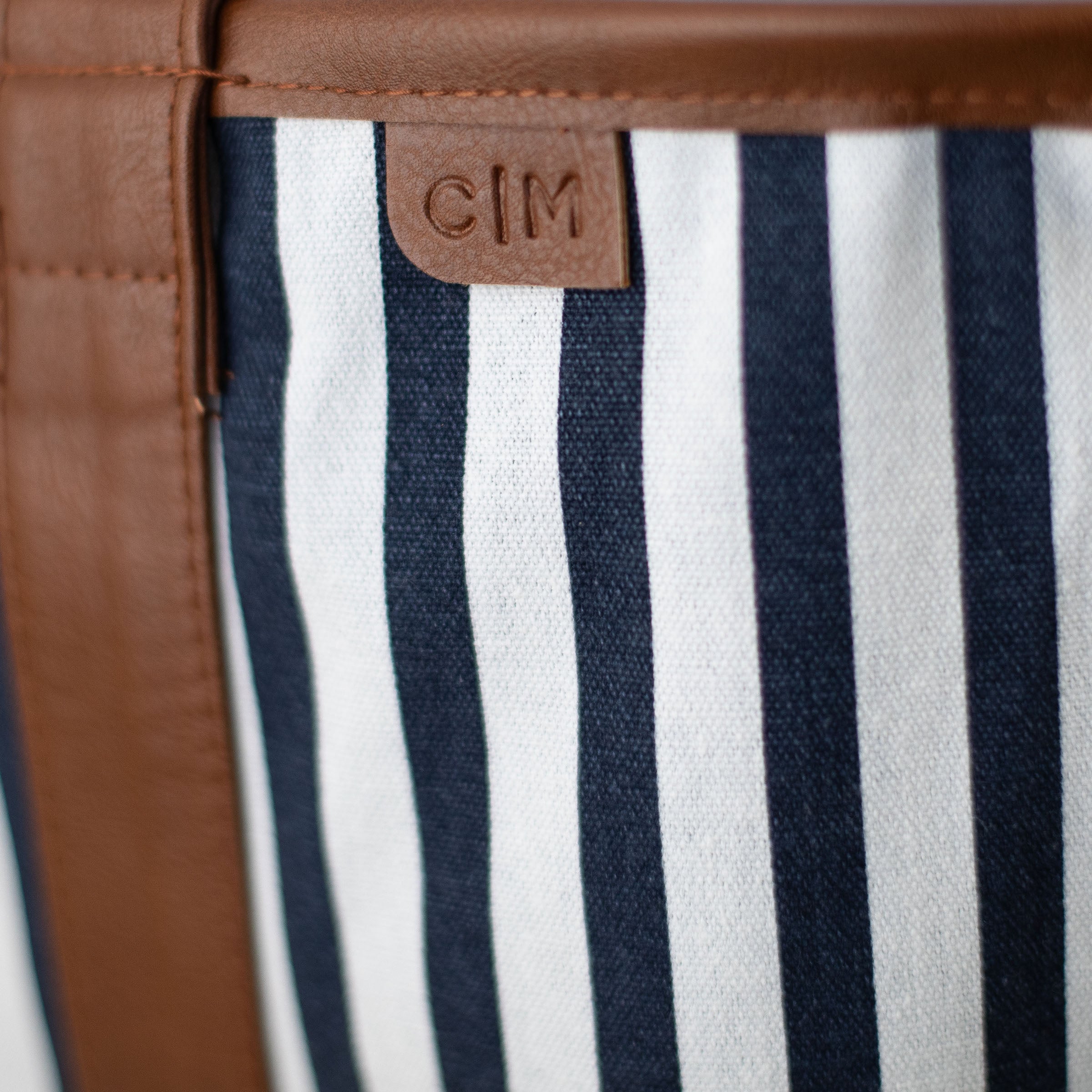 Close-up of a tote bag with striped fabric and brown leather trim, featuring the brand 'C|M'.