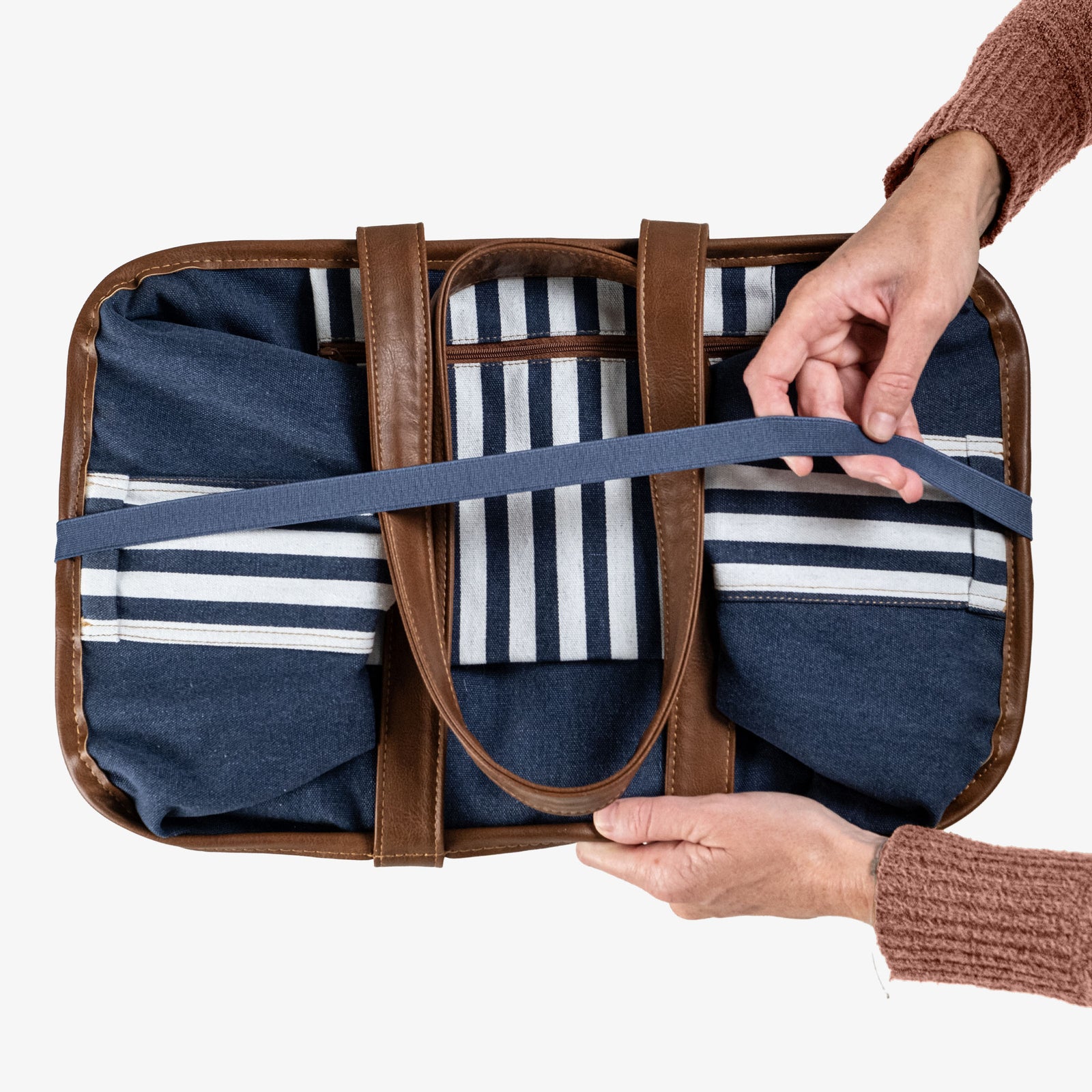 Person holding a folded blue-striped tote bag on a white background