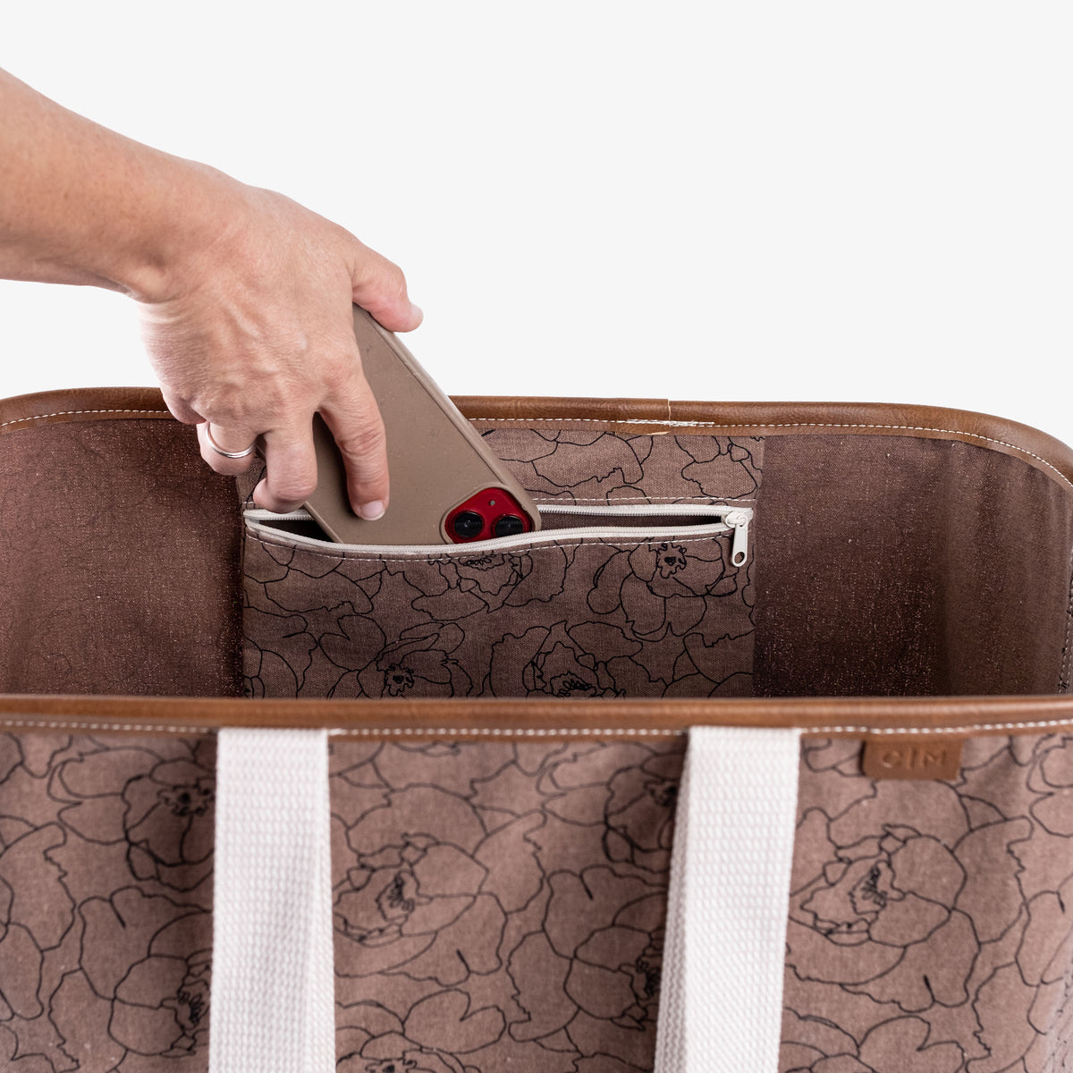 Brown floral-patterned bag with a hand opening a zipper pocket on a white background