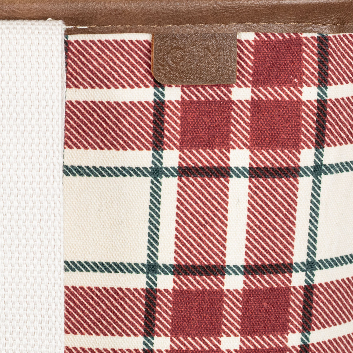 Close-up of a red and white plaid patterned tote bag with a brand label on a brown background.