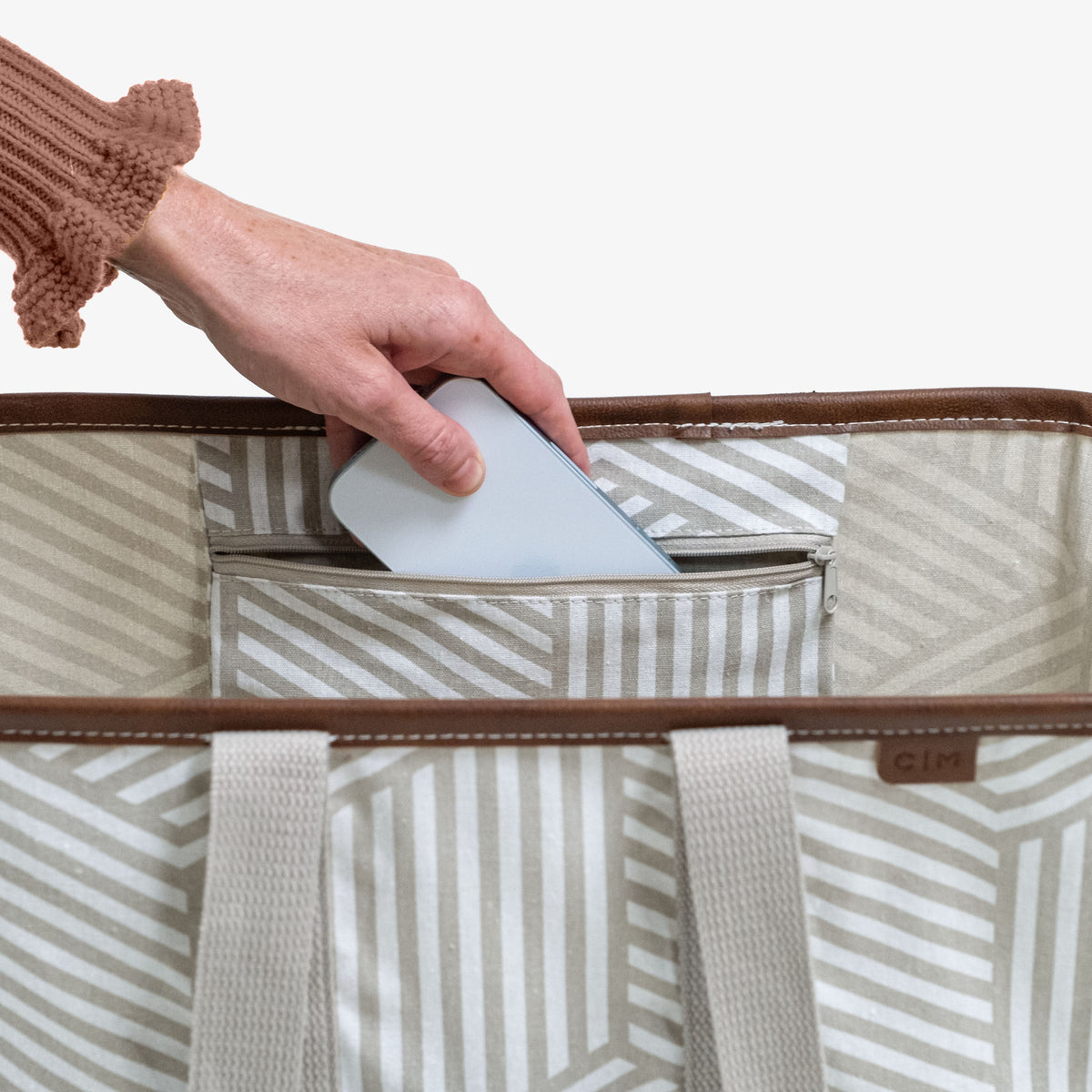 Hand placing a white phone into a striped tote bag with a brown trim.