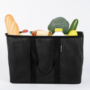 Black reusable shopping bag filled with groceries on a white background
