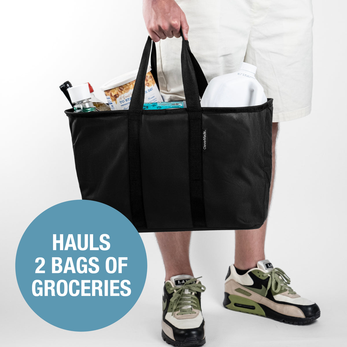Person holding a black pop-up tote bag filled with groceries on a white background