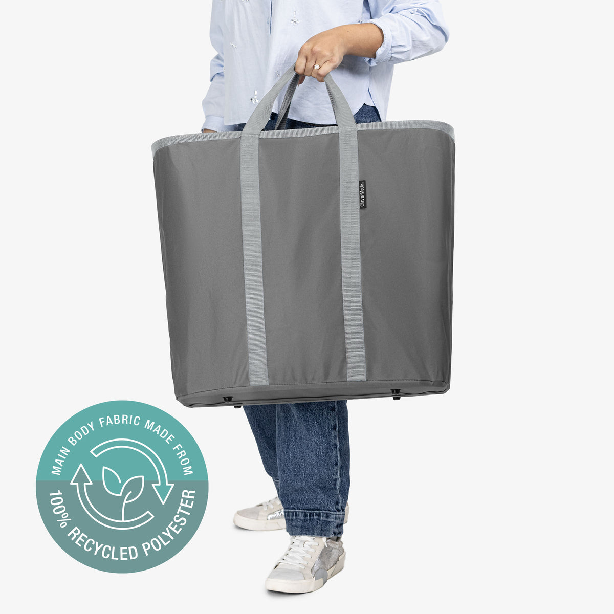 Person holding a large gray tote bag with a recycling logo on a white background