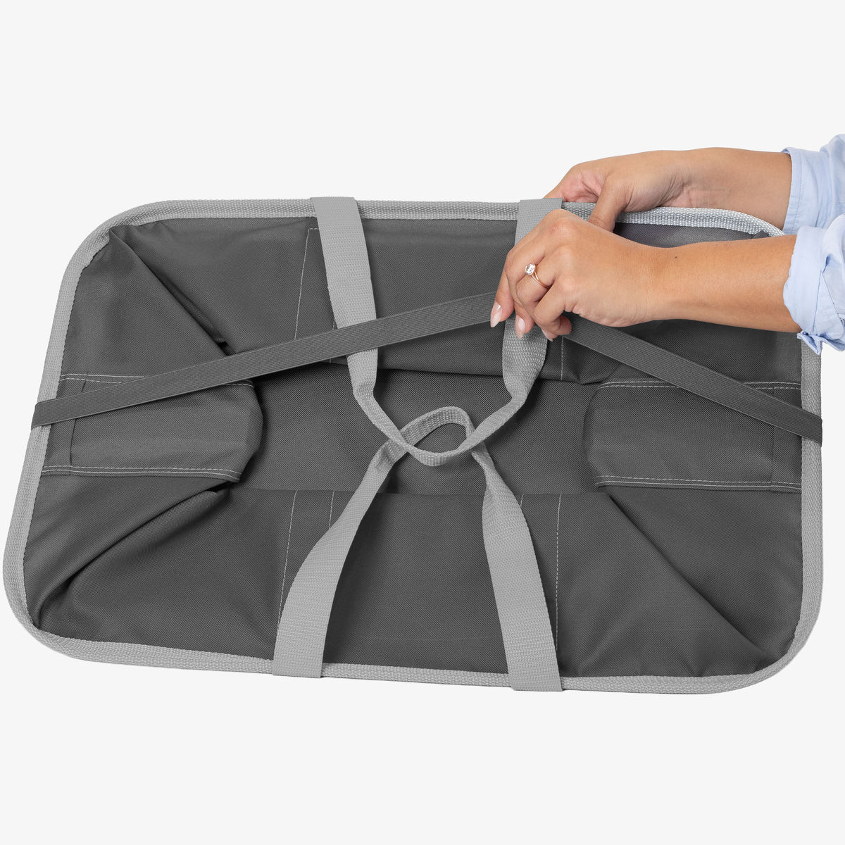 Person securing a gray and green laundry caddy with straps on a white background